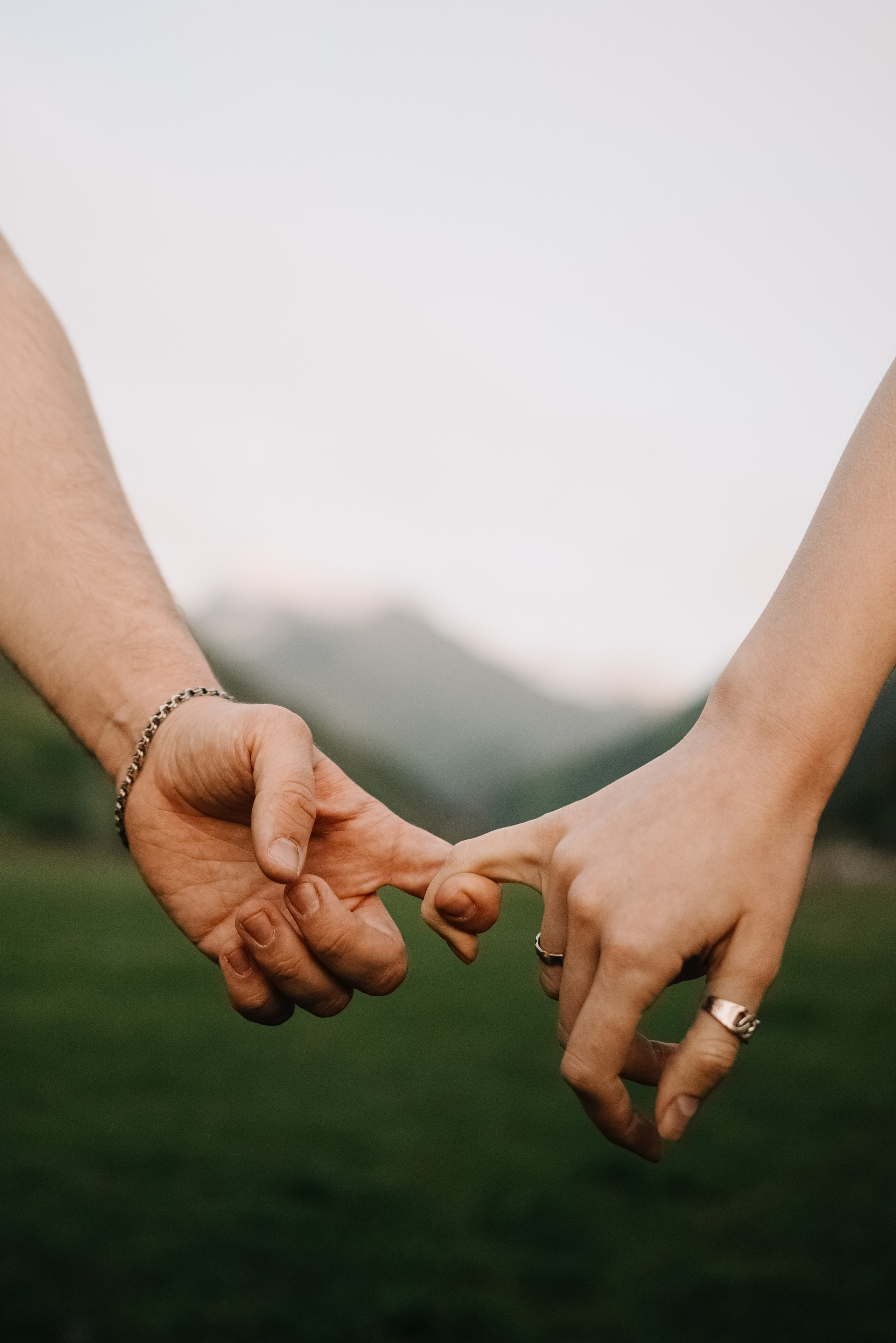 Фотография рук двух влюбленных, держащихся друг за друга указательным пальцем и мизинцем на фоне гор Казбеги