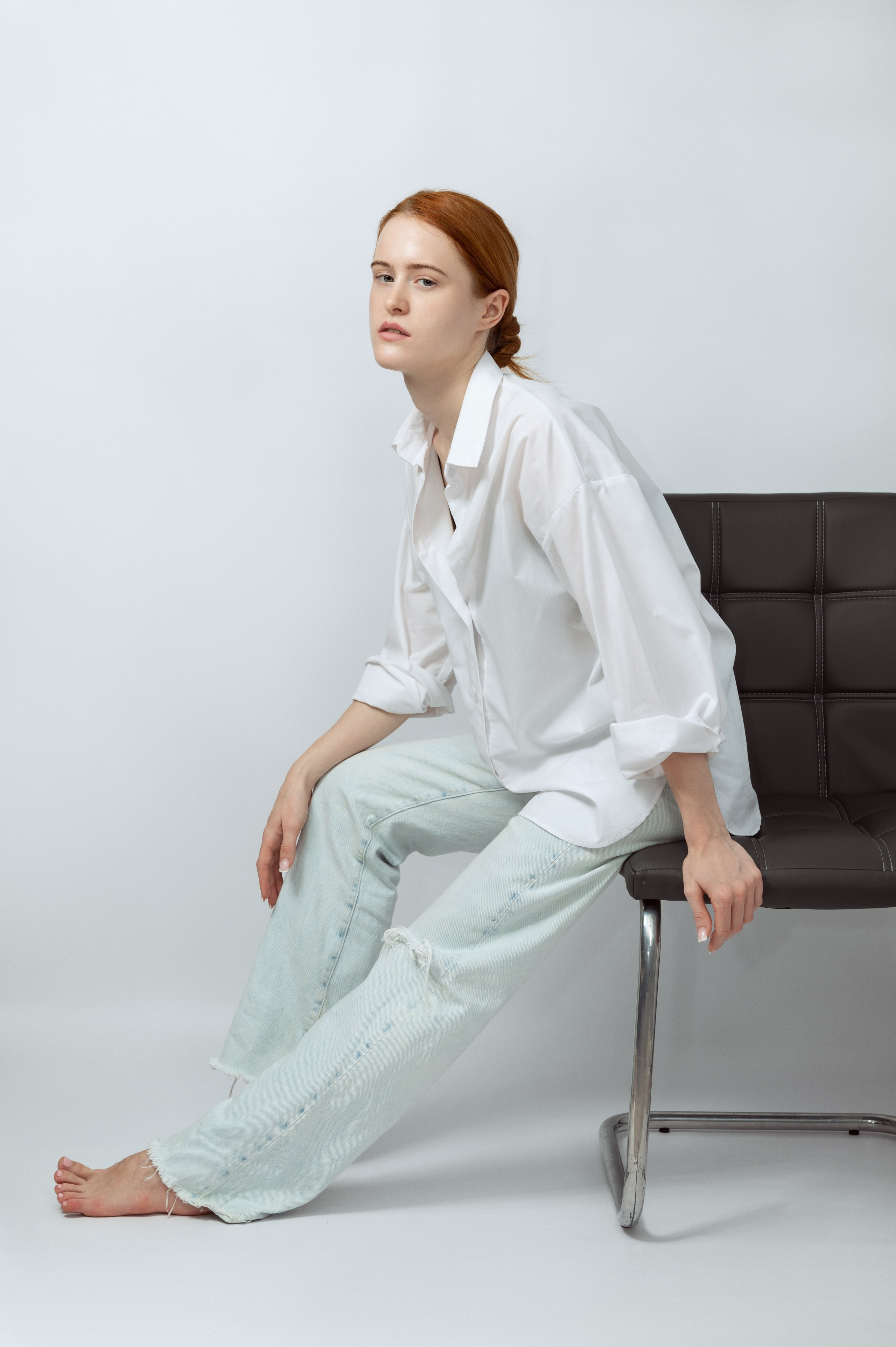 Рыжеволосая девушка-модель в белой рубашке и светлых джинсах на светлом фоне. Модельные тесты