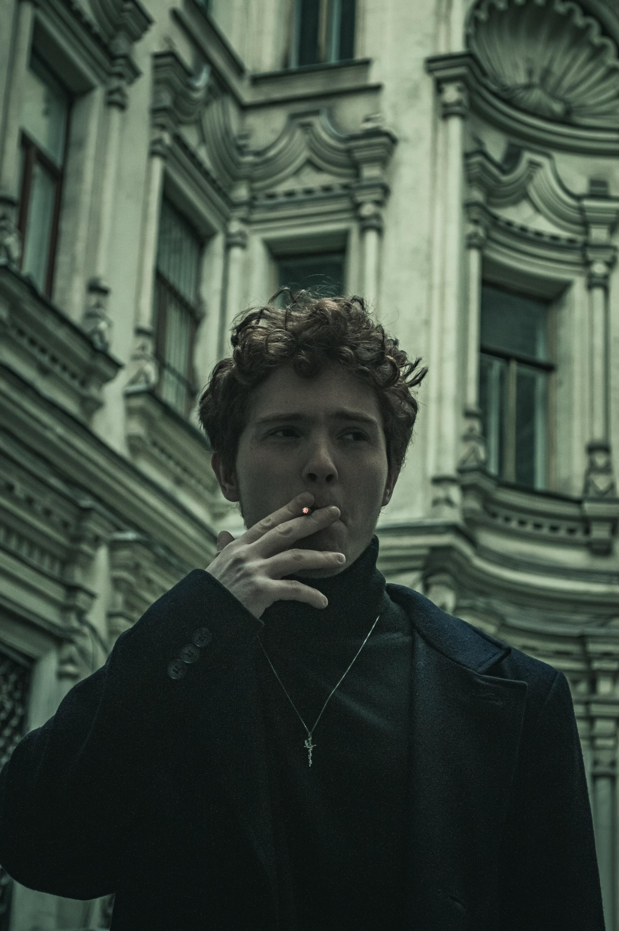 Уличный портрет рыжего курящего парня на фоне красивого здания.