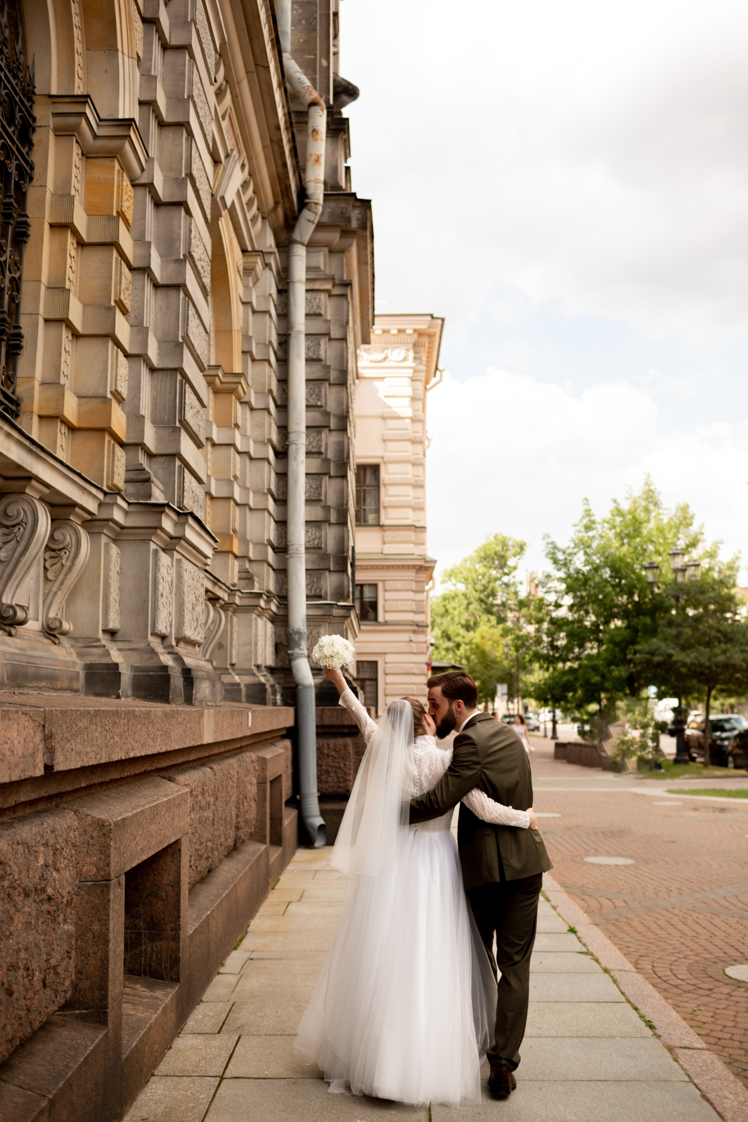 Невеста в белом обгятивающем платье с фатой машет букетом