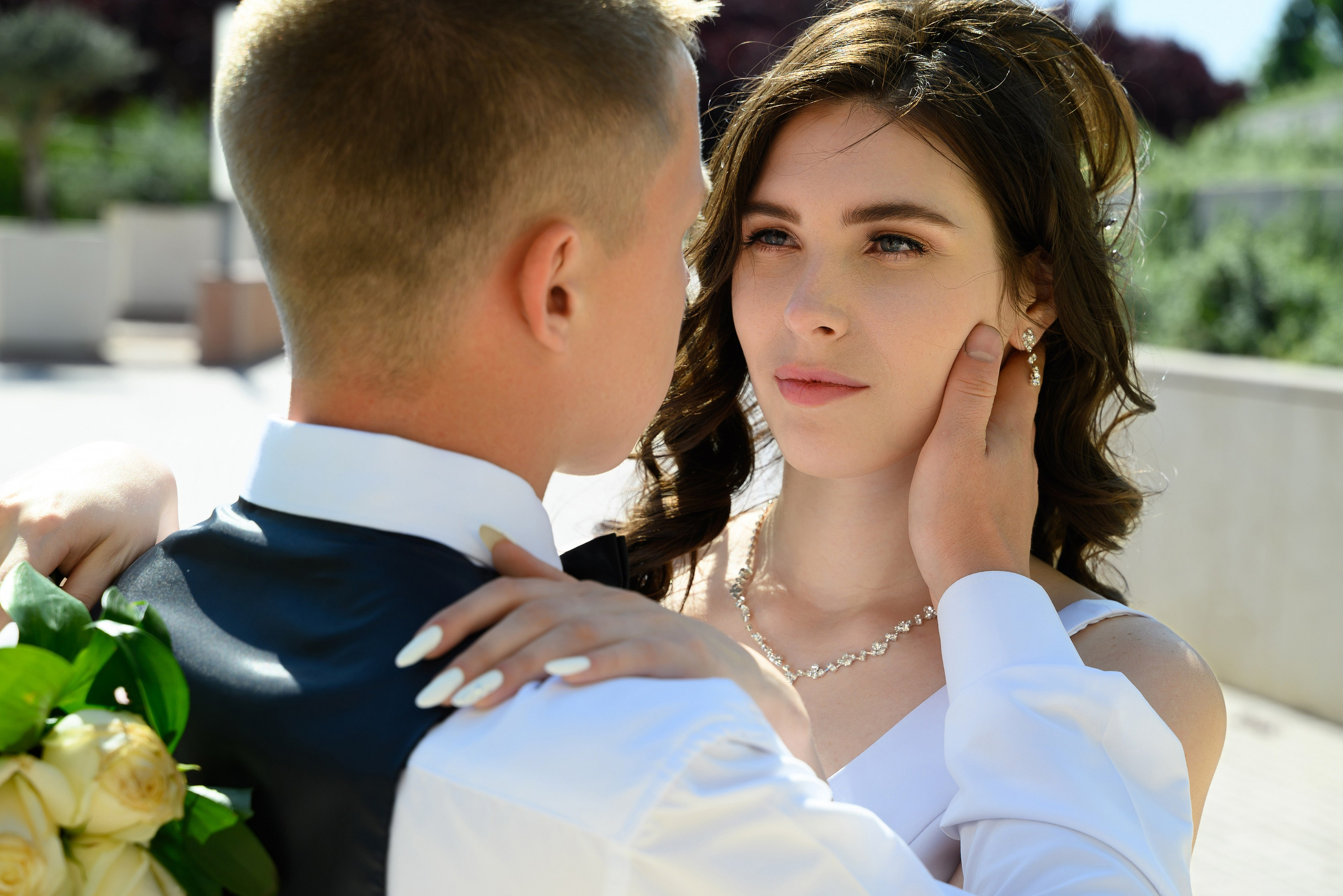 Жених обнимает невесту, кладет ей руку на шею и нежно с любовью смотрит ей в глаза.