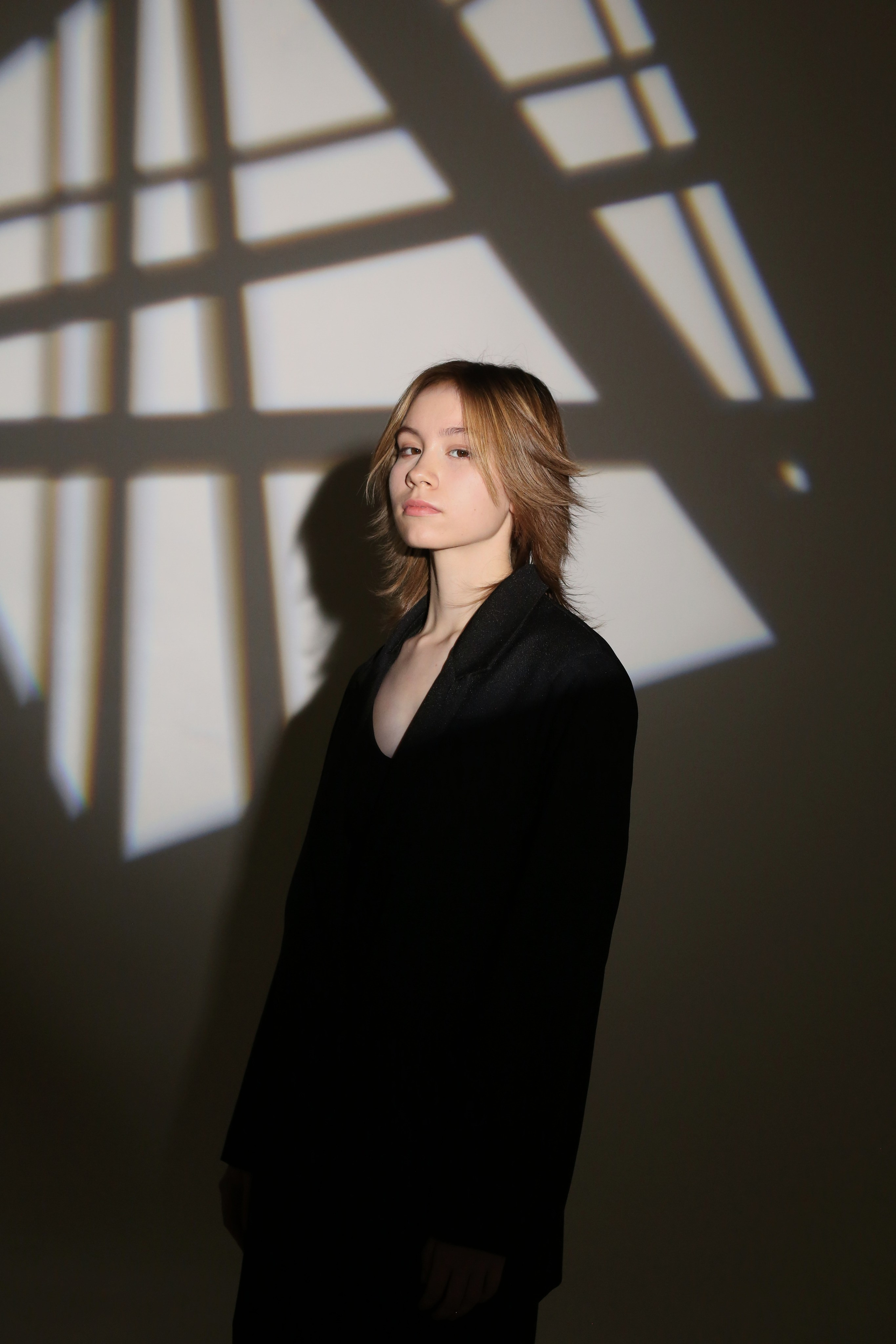 Студийная фотосессия «Геометрия»: девушка в черном костюме позирует в лучах света