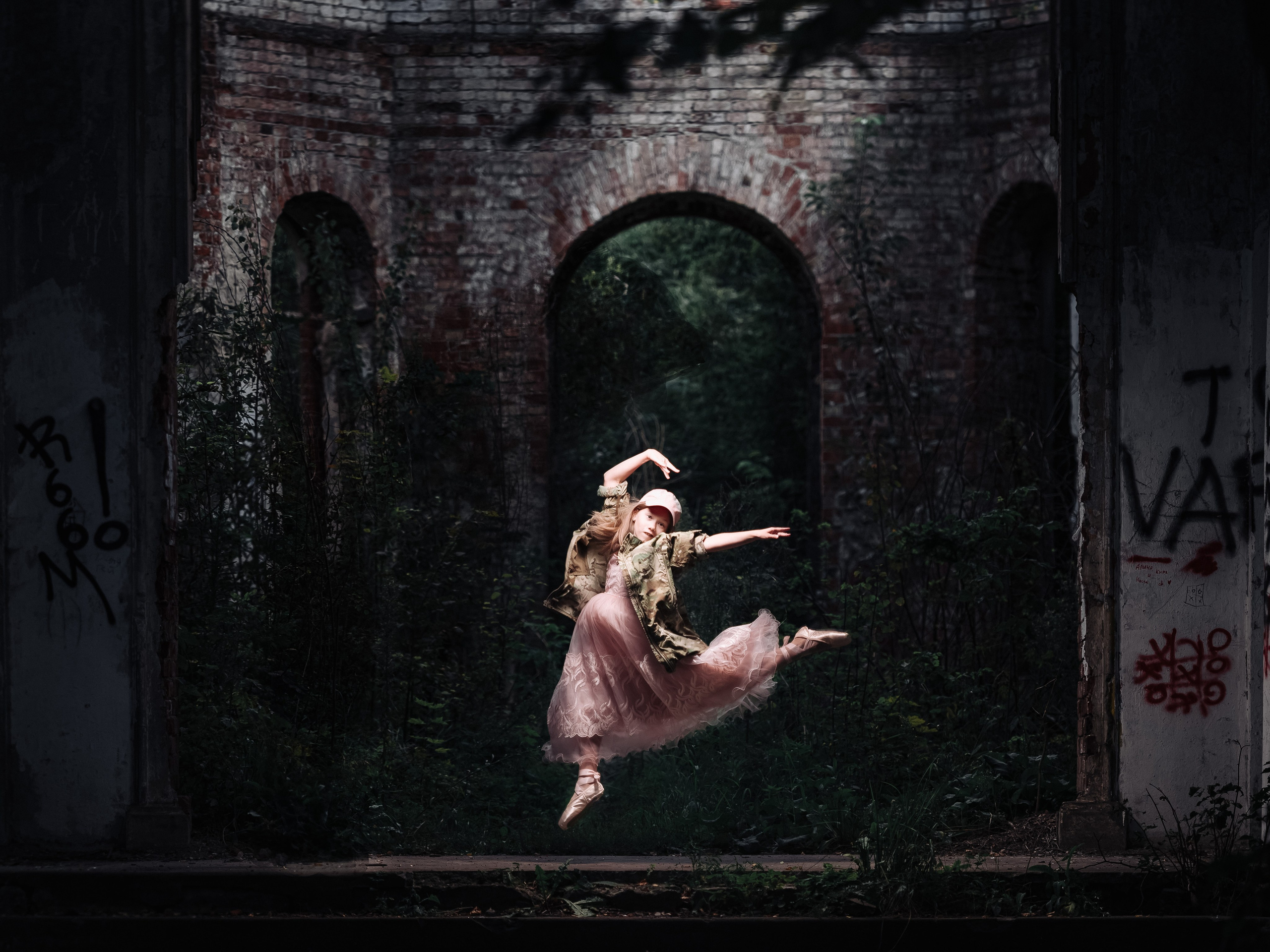 Девочка танцует в красивом платье и камуфляже на фоне кирпичной стены