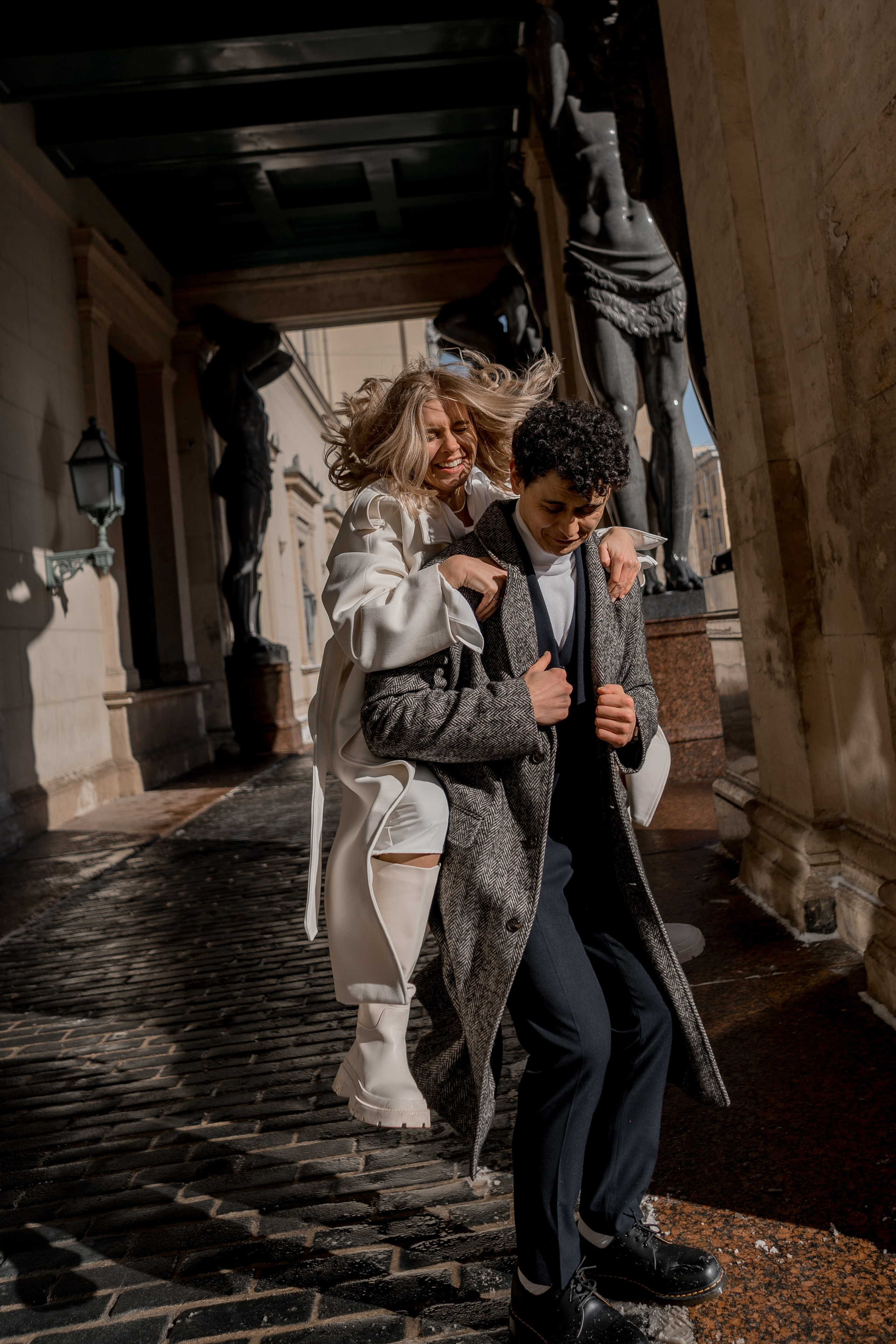 невеста со спины запрыгивает на спину жениху около атлантов эрмитажа