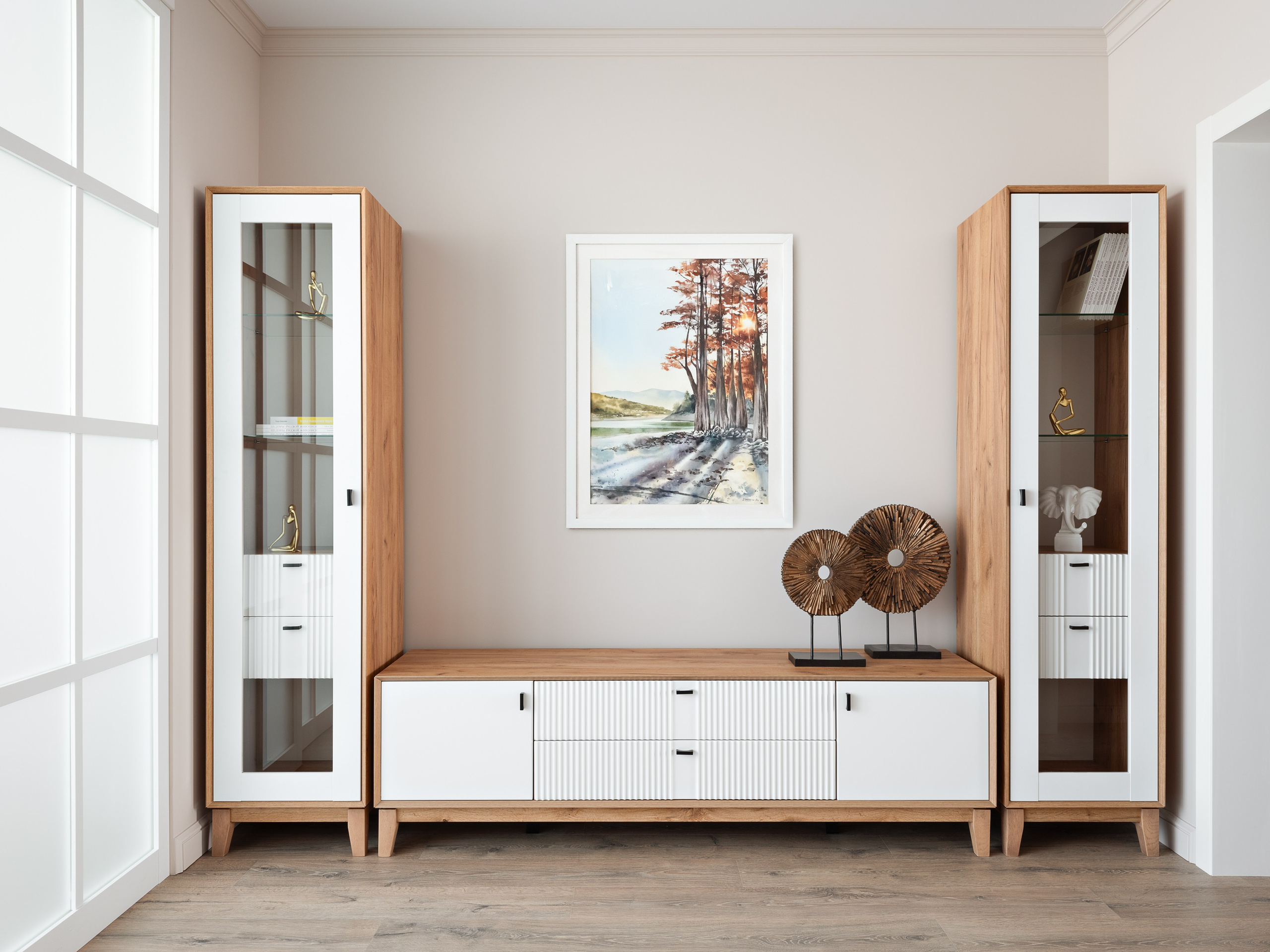 Просторная гостиная с симметричной расстановкой мебели: две витрины из дерева и белого фасада, центральный комод, картина с природным пейзажем и декоративные элементы. Атмосферу создали дизайнер Наталья Бунеева, стилист Наталья Якушева, фотограф Сергей Денисенко.