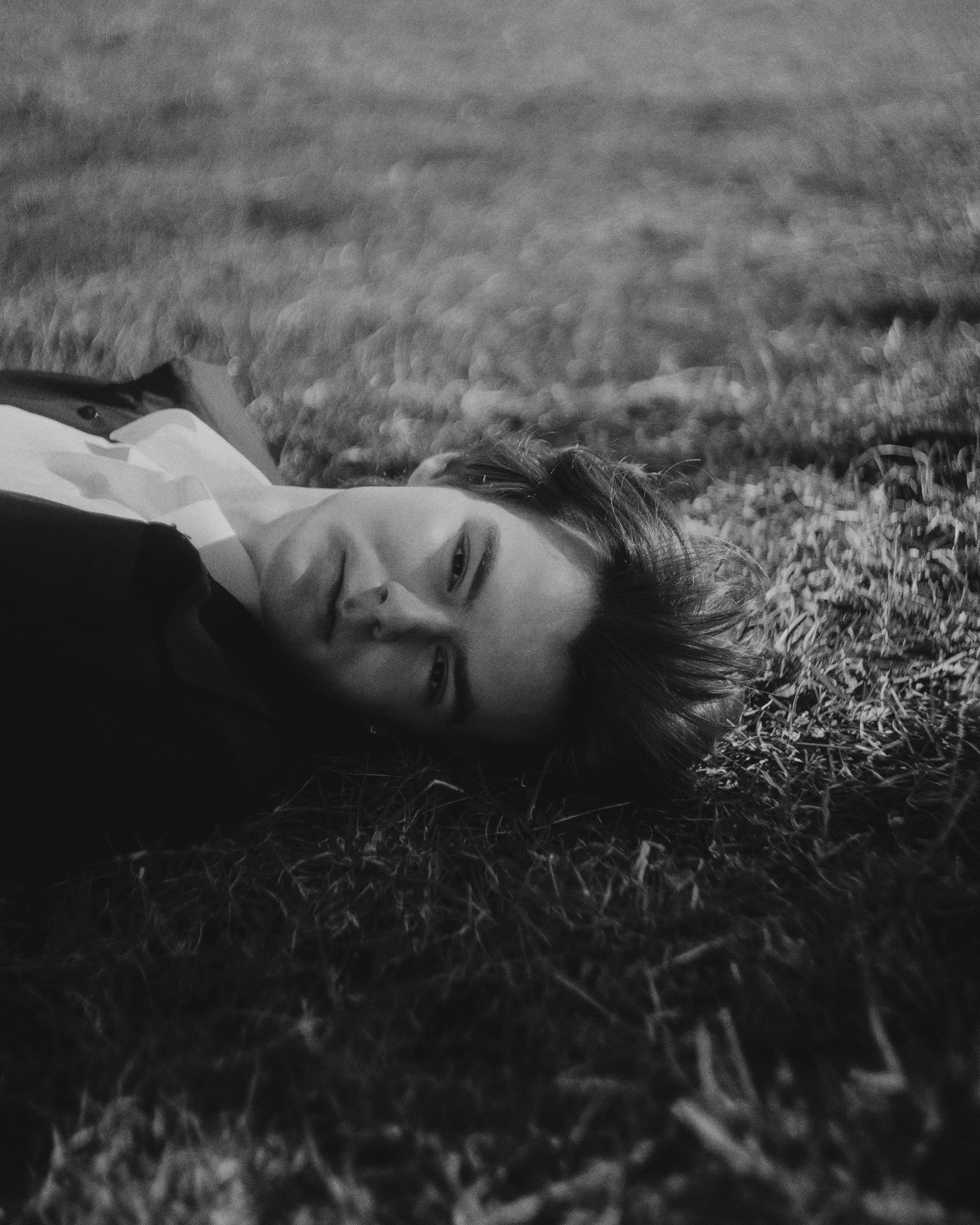 черно-белый мужской портрет, мужчина лежит на траве в классической рубашке, контрастный свет, фотосессия в стиле нуар