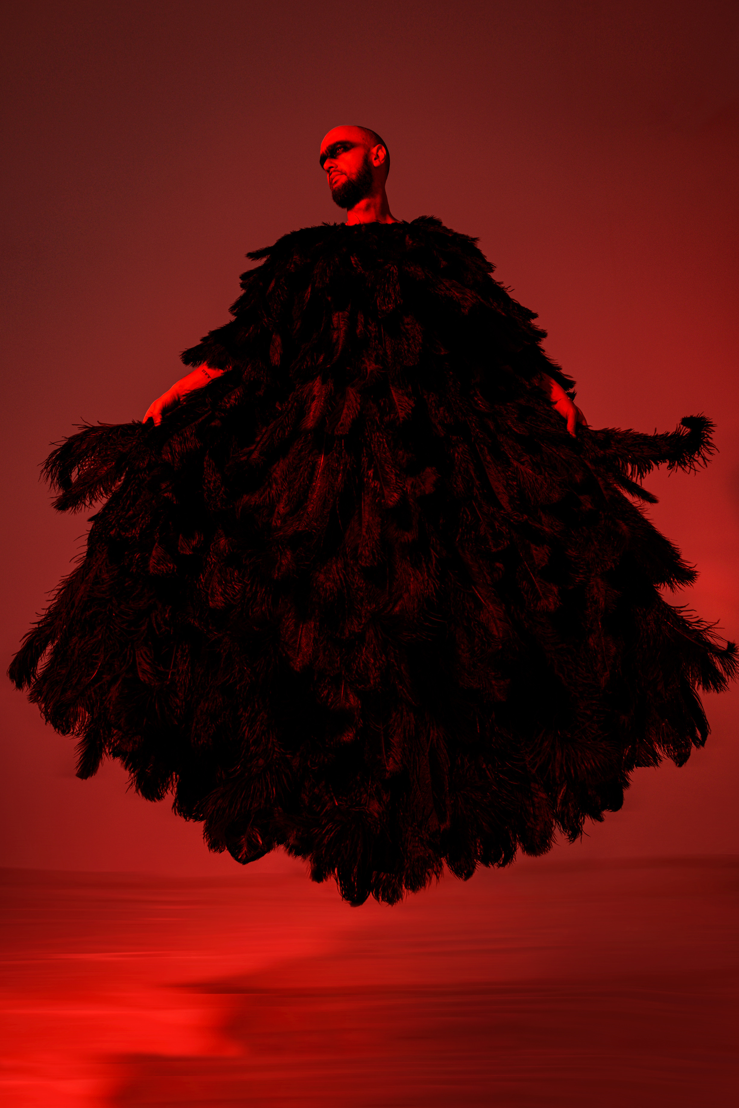 мужчина в накидке из перьев в цветном свете и черным гримом