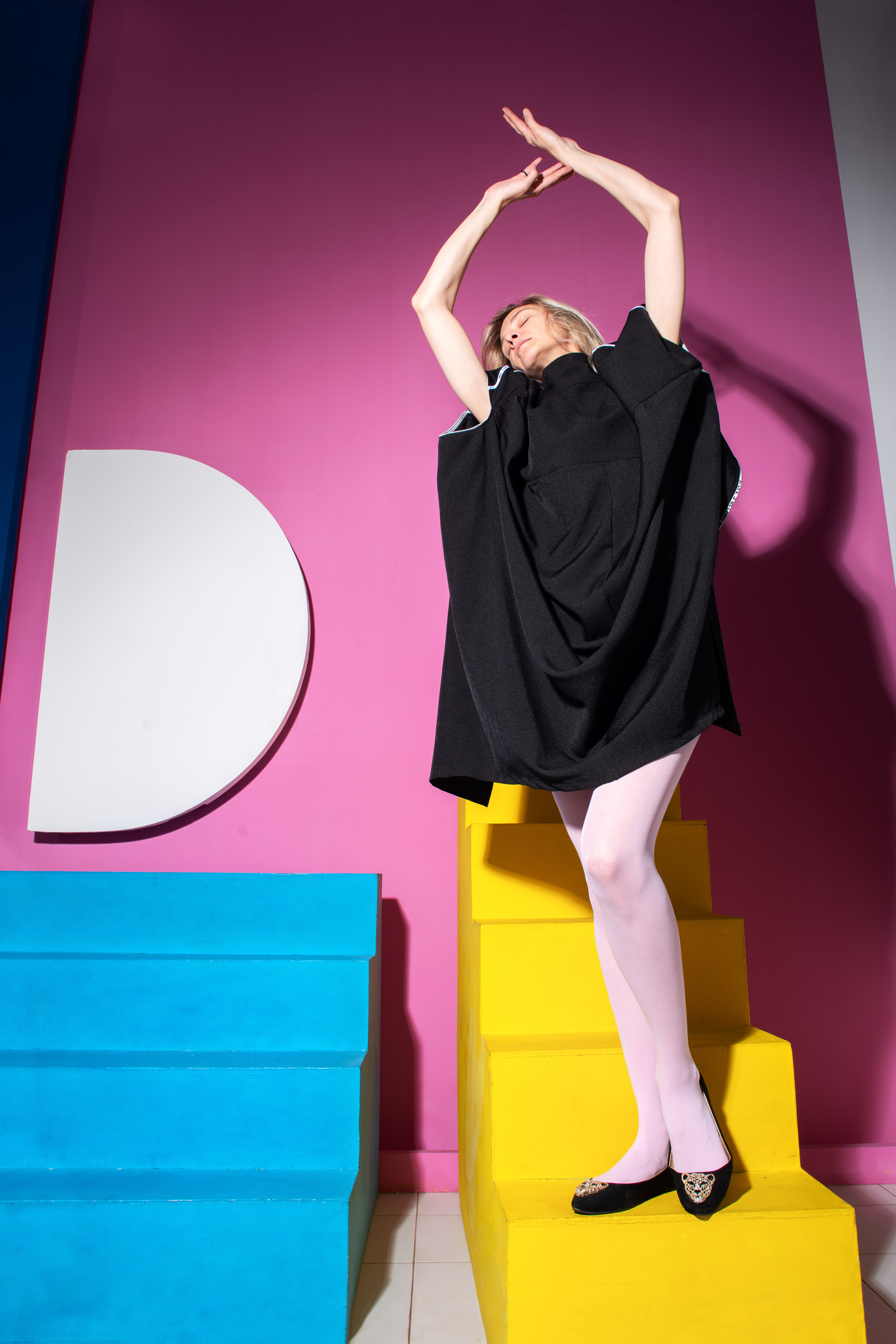 девушка в студии в черном платье на фоне разноцветных геометрических фигур 