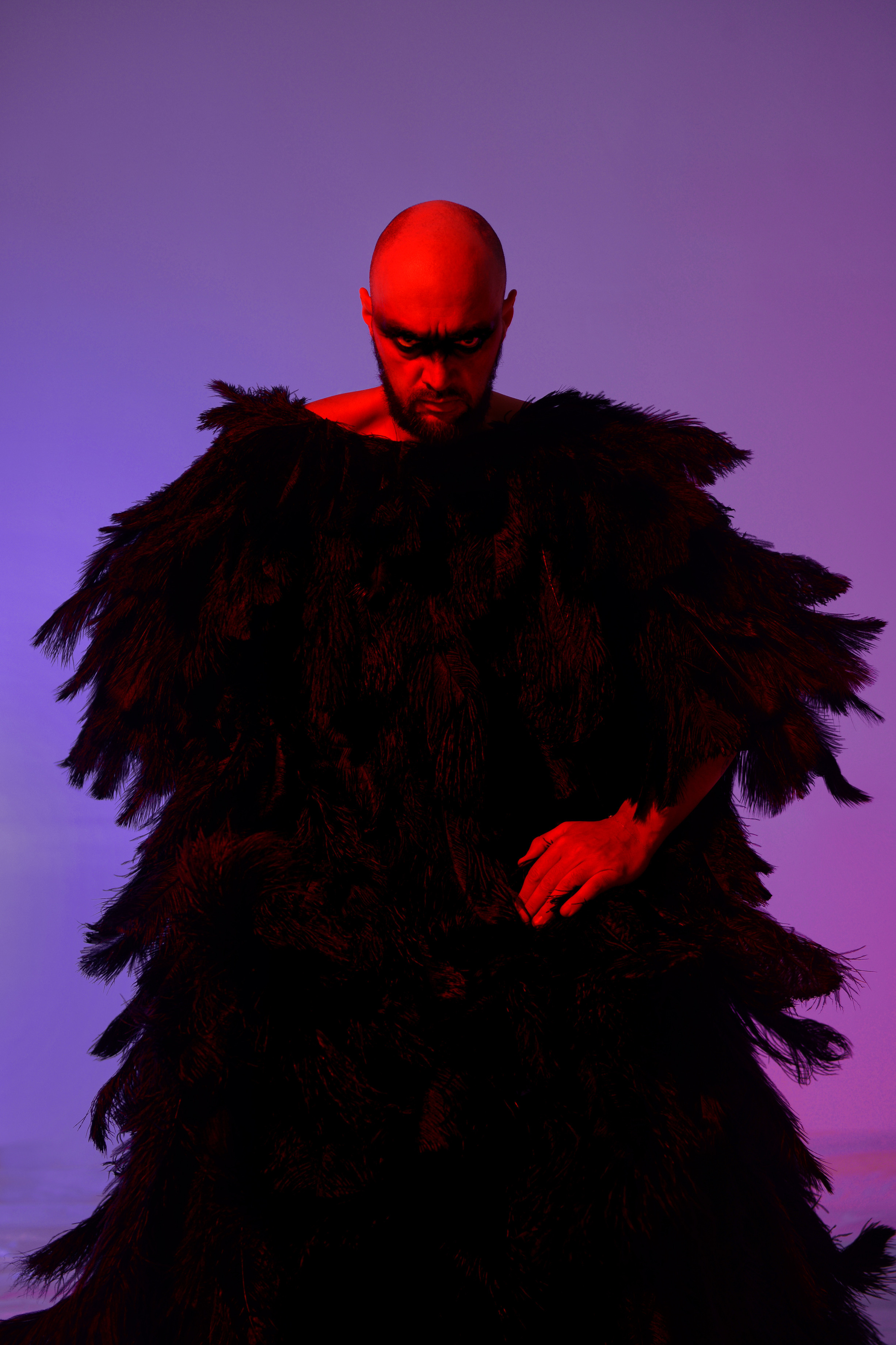 мужчина в накидке из перьев в цветном свете и черным гримом