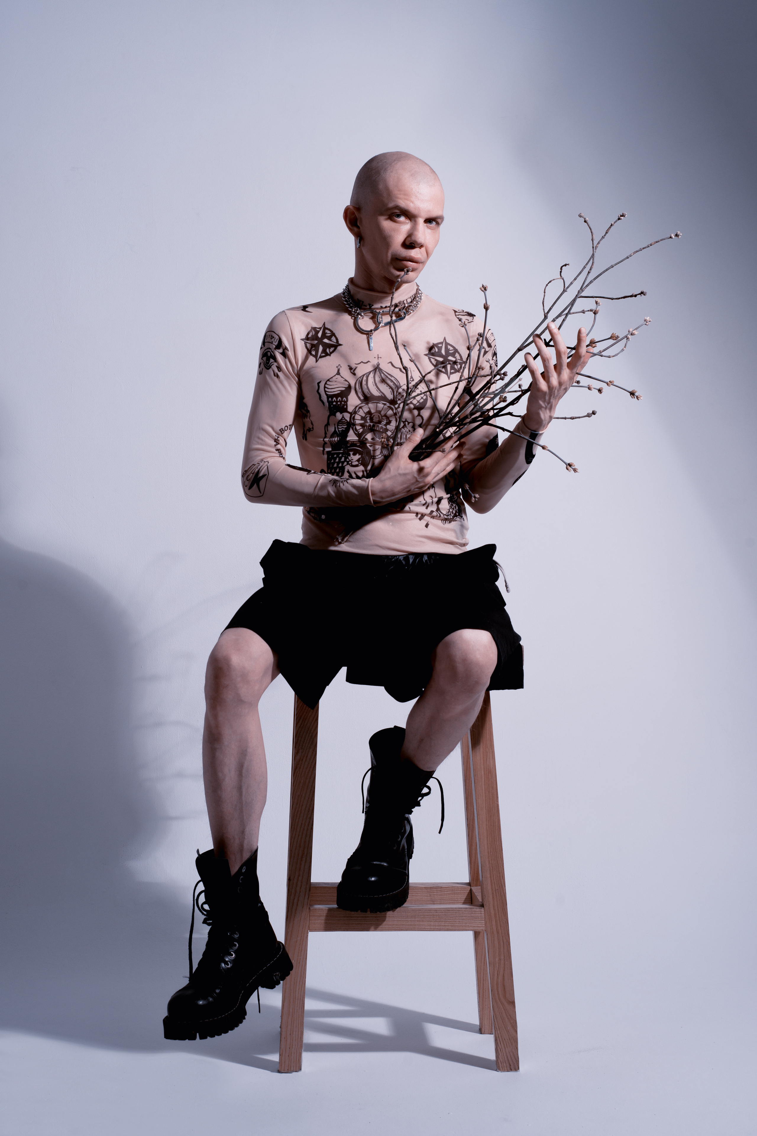 лысый мужчина в татуировках сидит на высоком стуле и держит ветки 