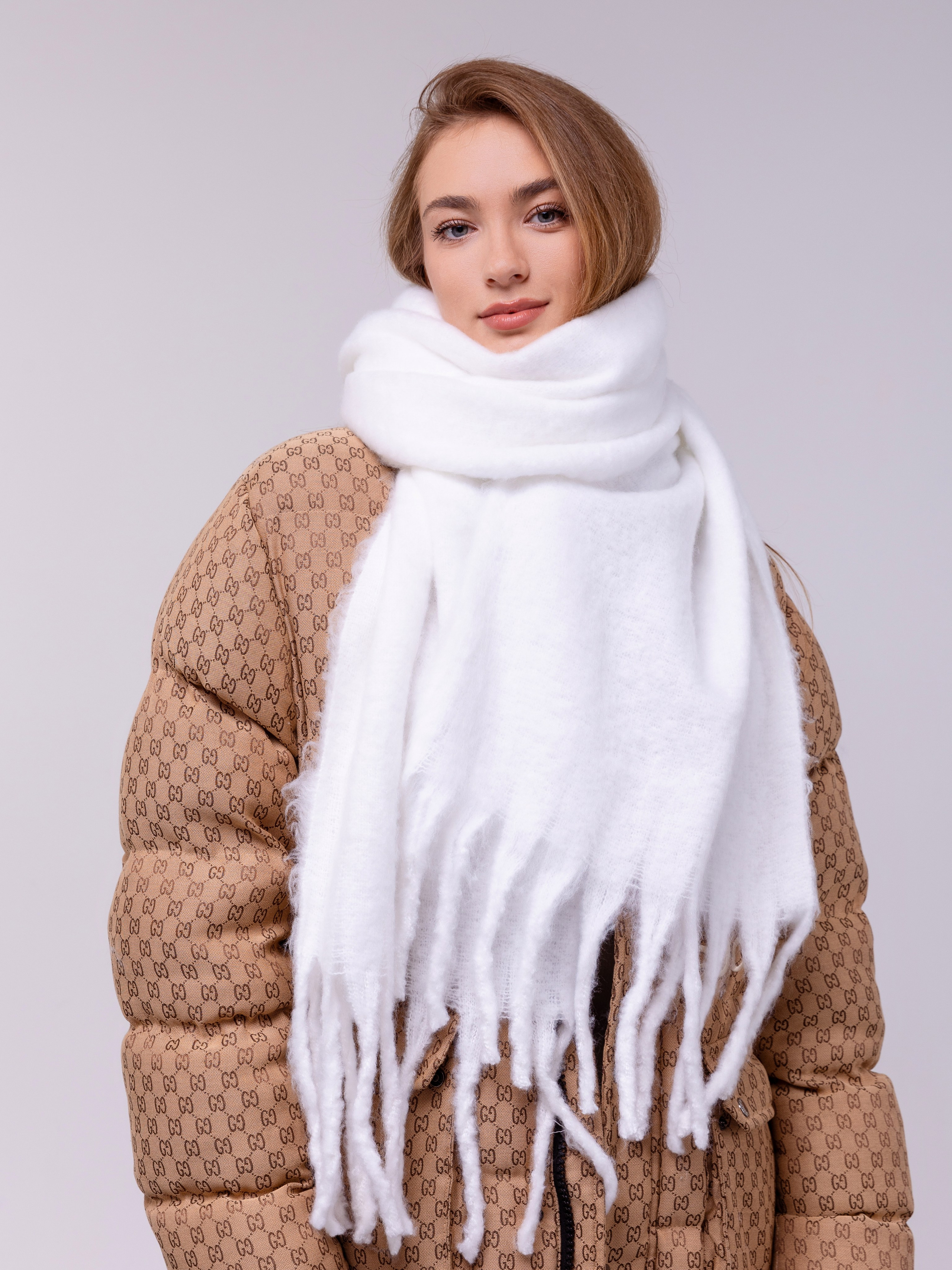 Белый шарф обвязан у девушки вокруг шеи и спускается на грудь.