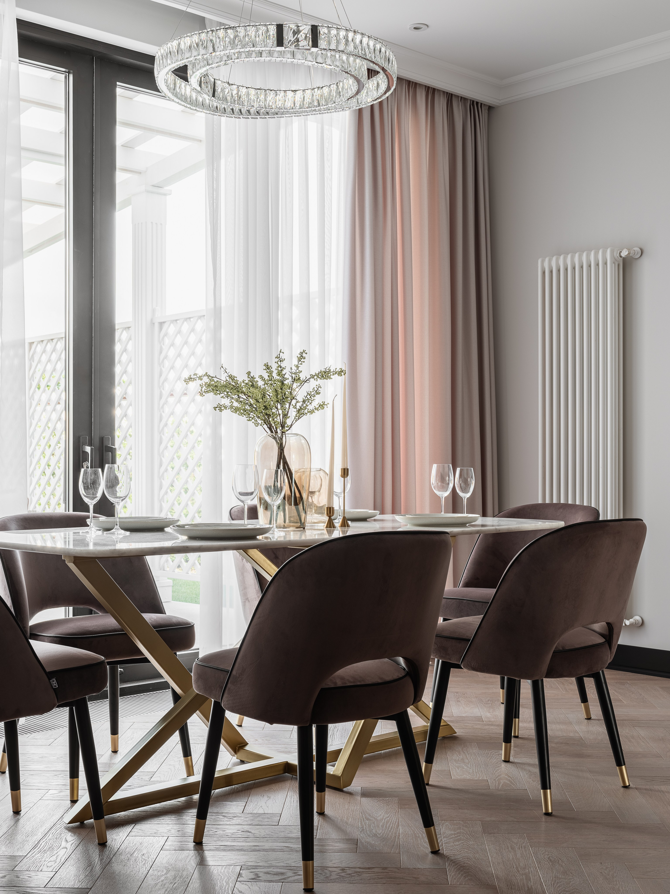 Уютная столовая зона с круглым обеденным столом на золотом основании и мягкими стульями шоколадного оттенка. Хрустальная люстра и длинные шторы создают атмосферу уюта, интерьер Василиссы Бачевой, стилист Наталья Якушева, фото Сергей Денисенко.