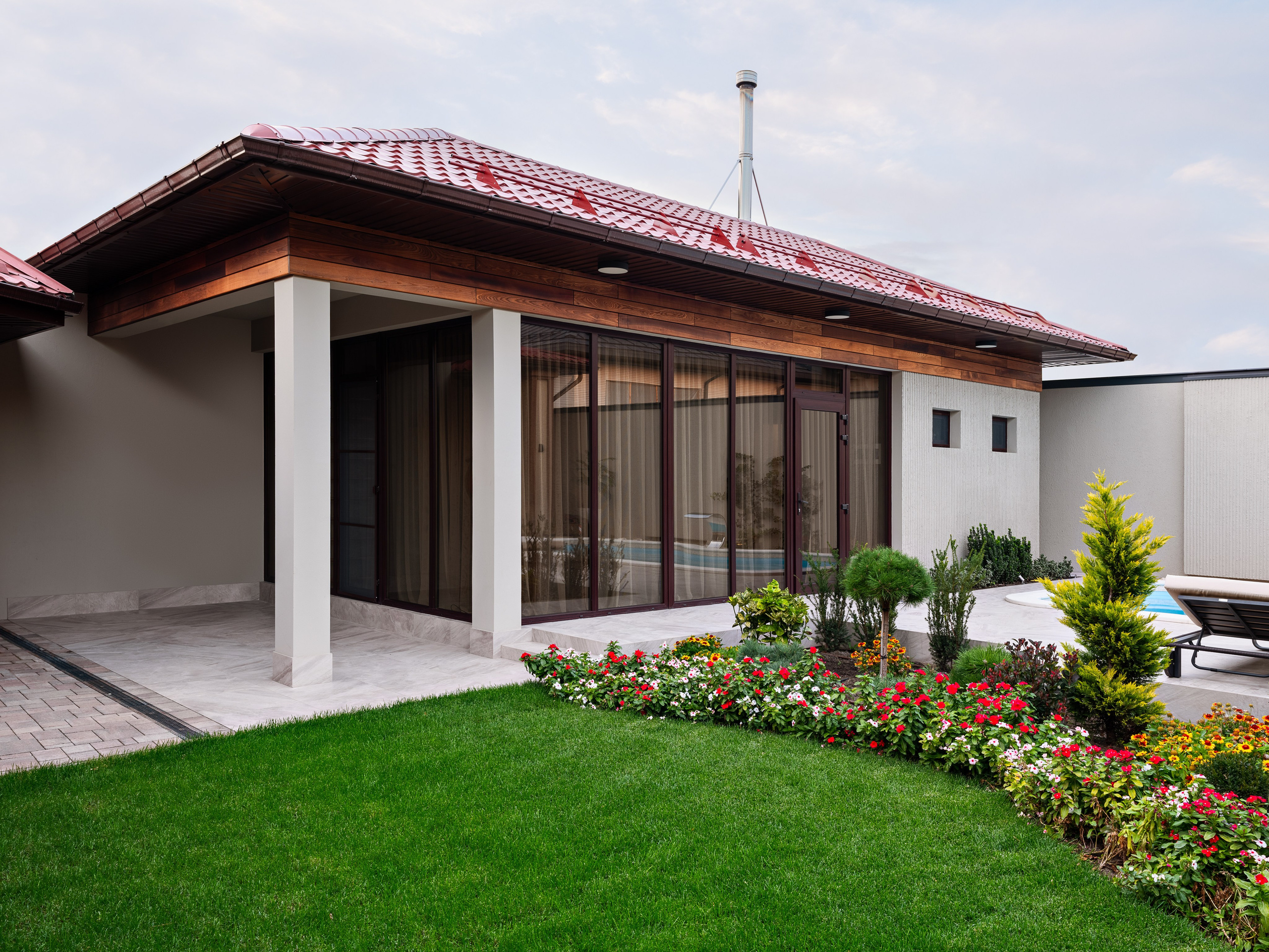 Современный фасад частного дома с панорамными окнами и аккуратным садом с цветочными клумбами, выполненный в проекте дизайнером Наталией Шелепниковой, стилист Софией Калбазовой и запечатленный фотографом Сергеем Денисенко в утреннем ракурсе.