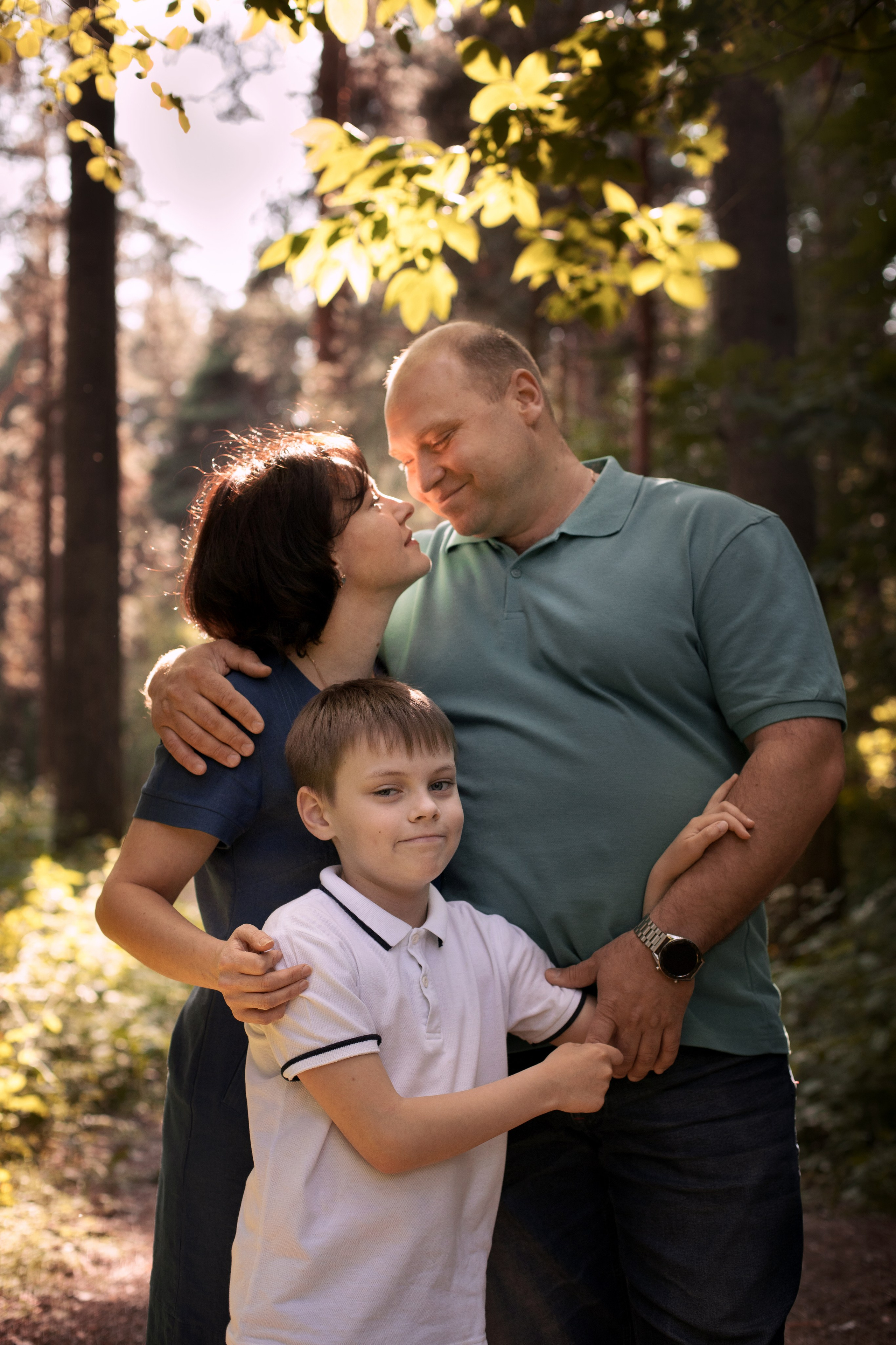 Семья - папа, мама, сын, обнимаются в летнем саду в контровом свете