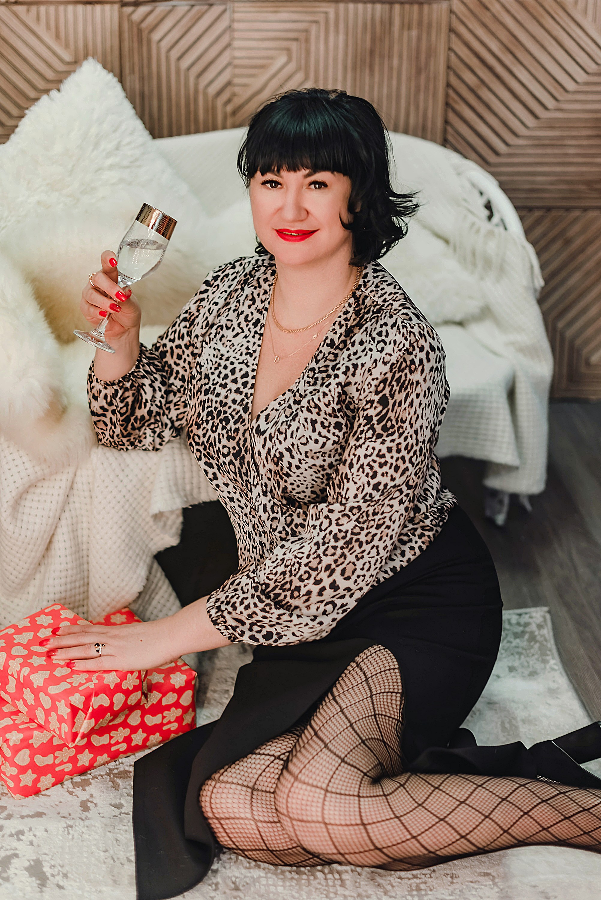 На фото девушка с подарком сидит около дивана.