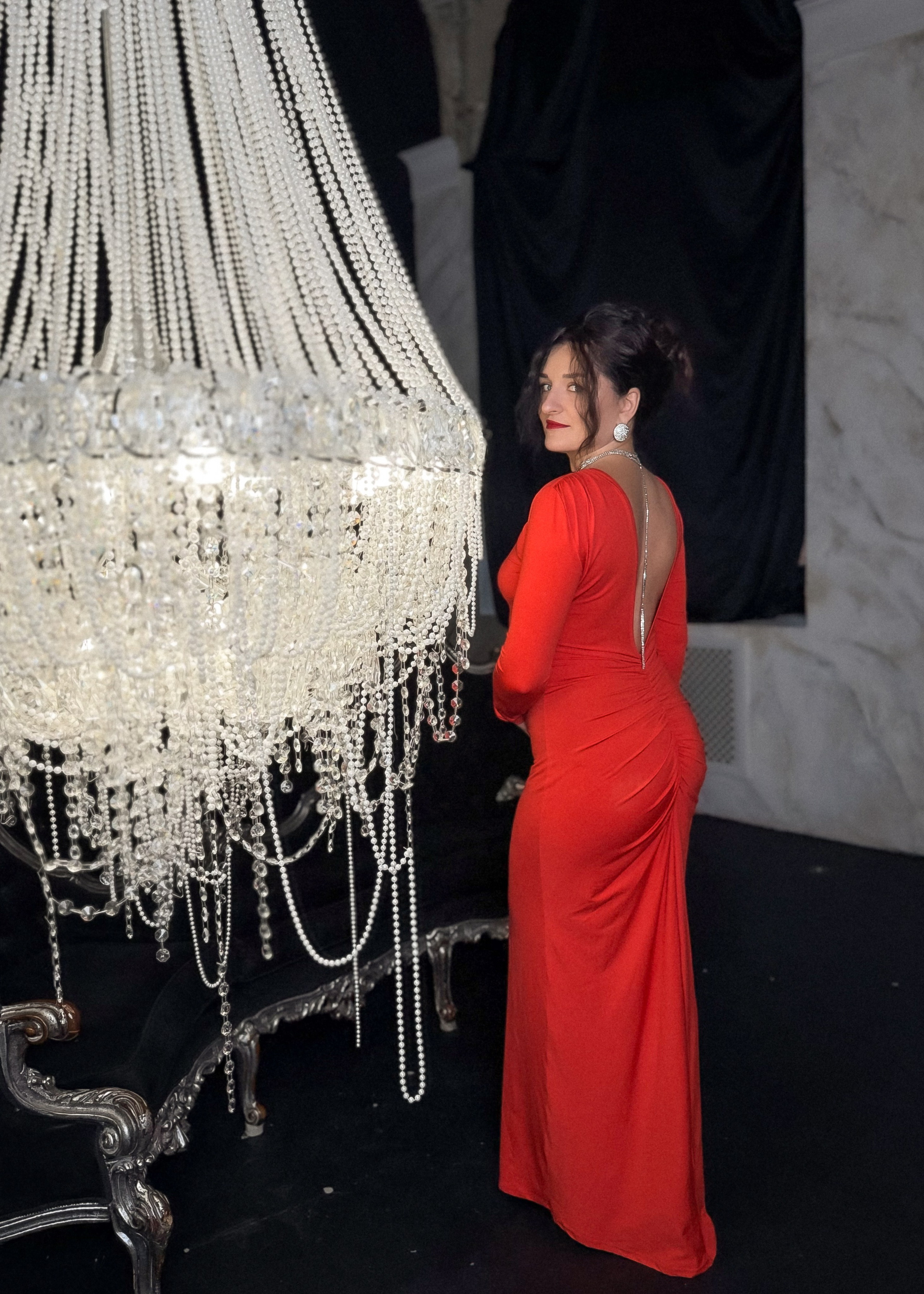 девушка в красном платье с люстрой в темном зале