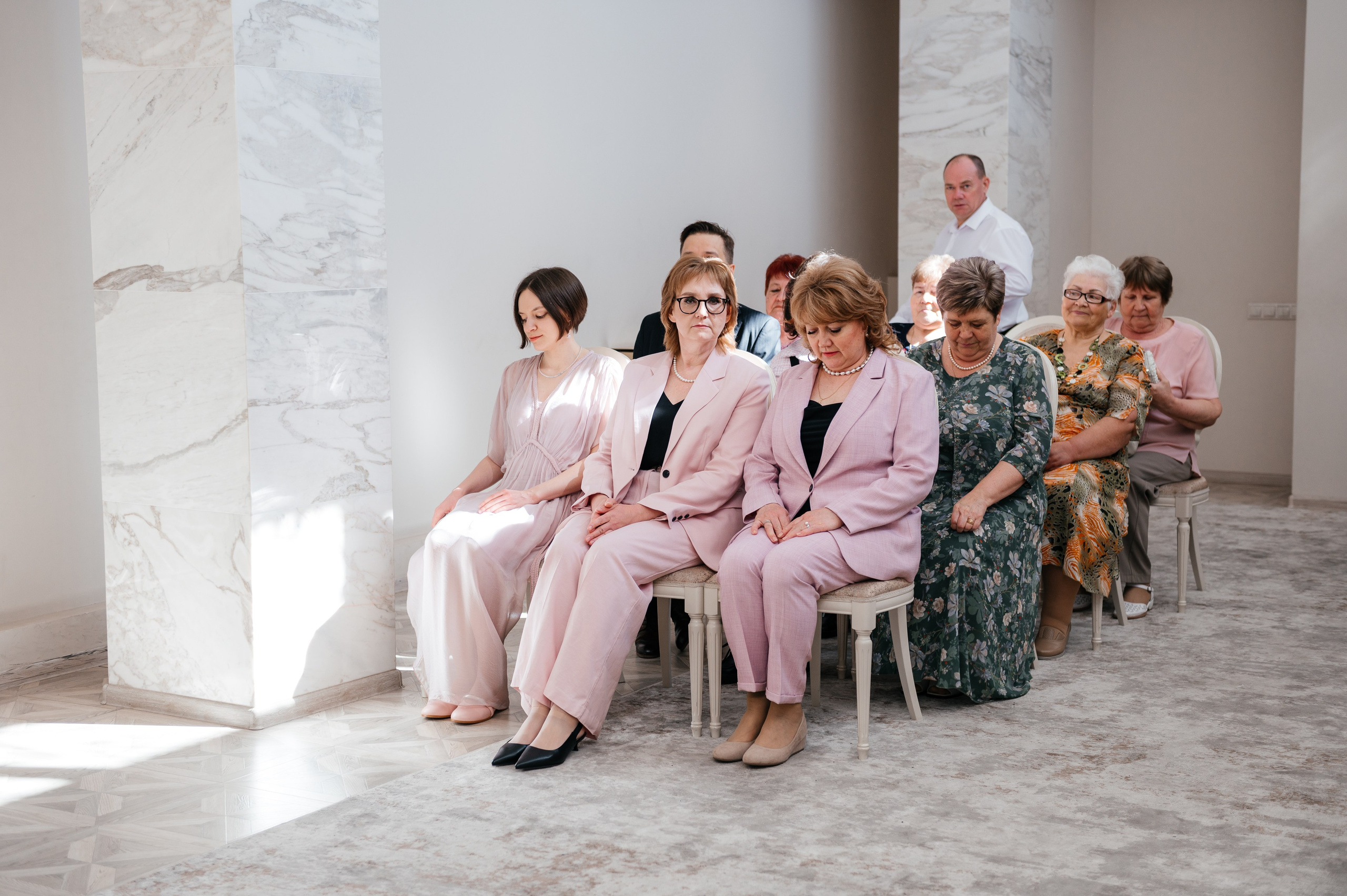 Родители сидят на стульях в первом ряду в загсе.