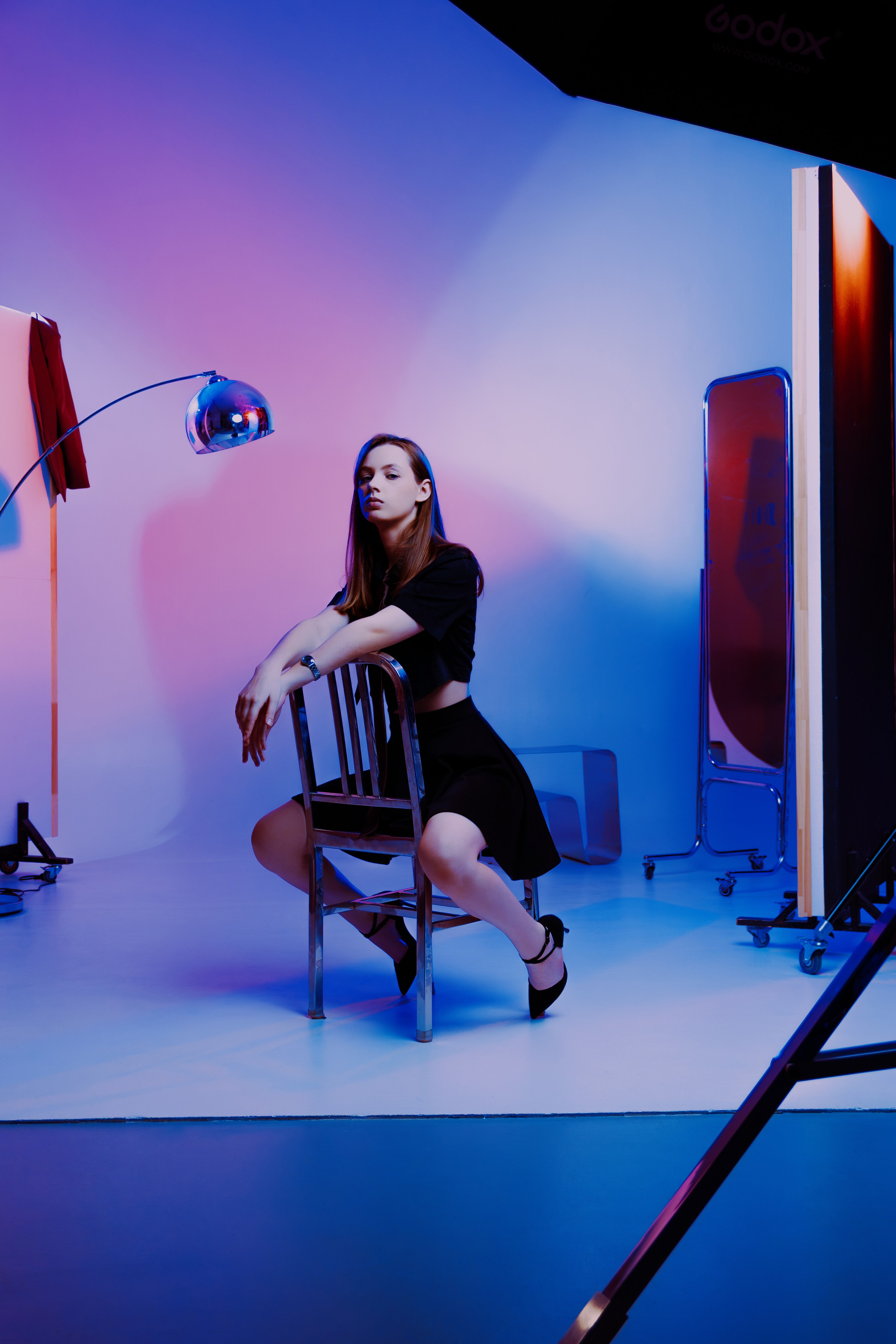 Модель в чёрном наряде на металлическом стуле: элегантность в сочетании с современным студийным светом. Градиентный фон подчёркивает образ.