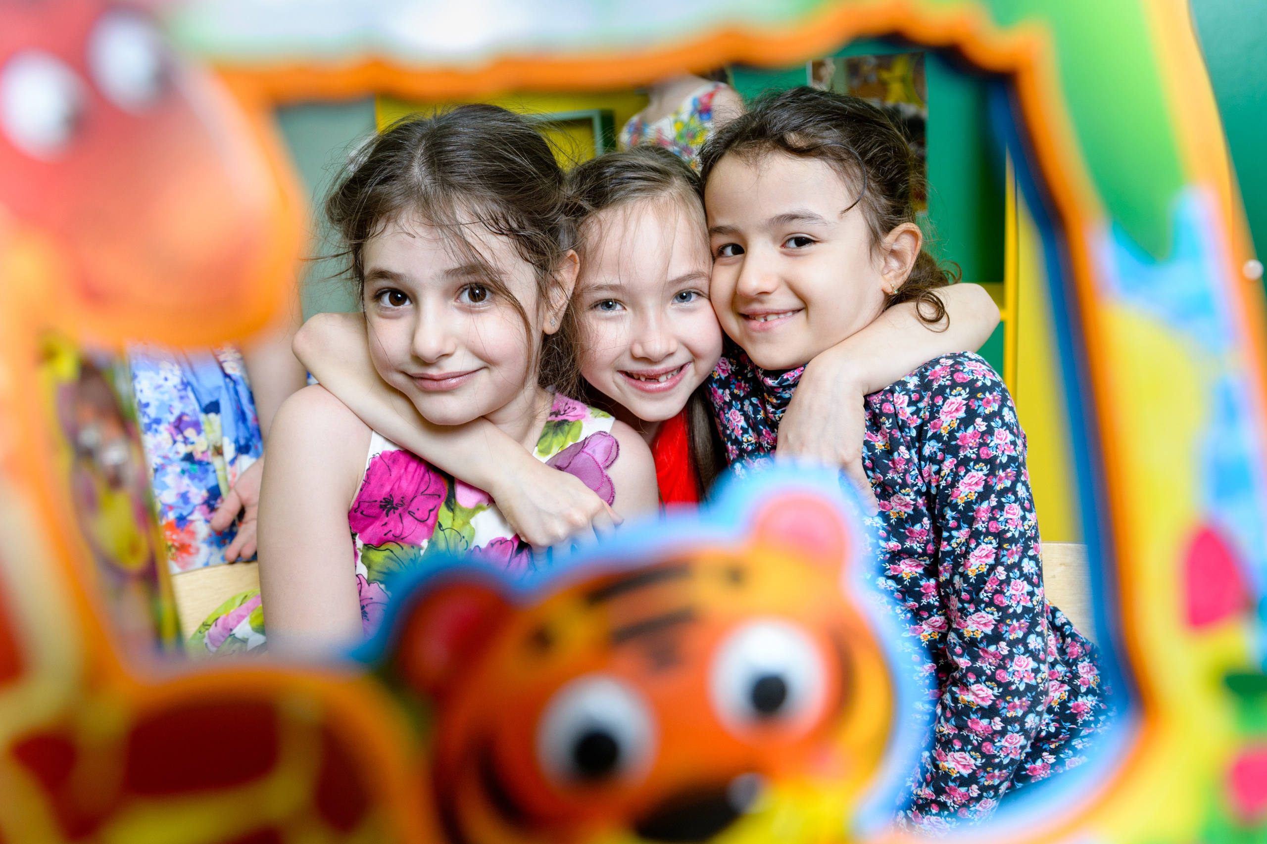 Трое девочек смотрят через окошко на обложке яркой детской книжки. 