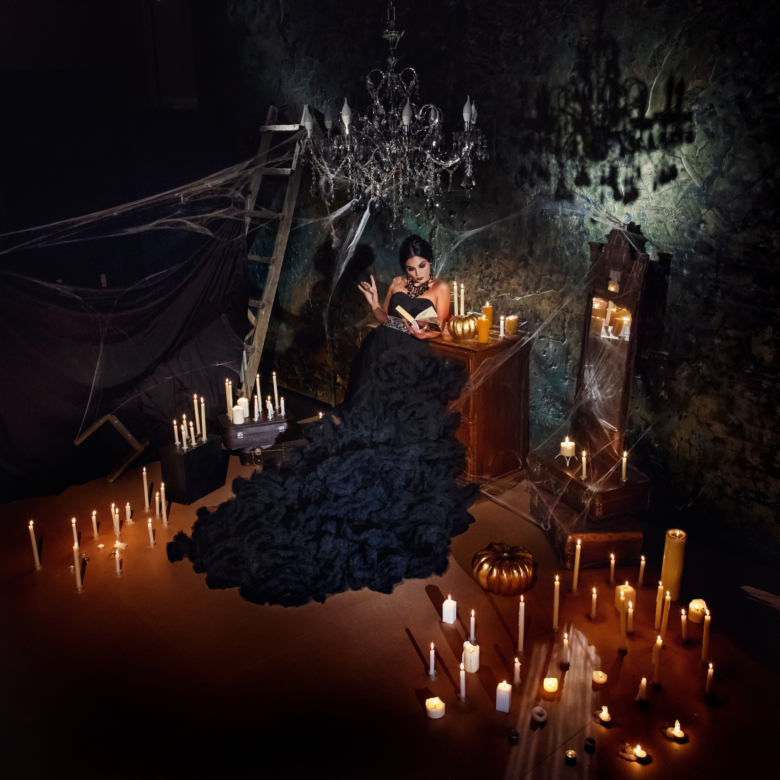 женщина в черном платье в атмосфере хэллуина в окружении свечей и тыкв на стенах висит паутина