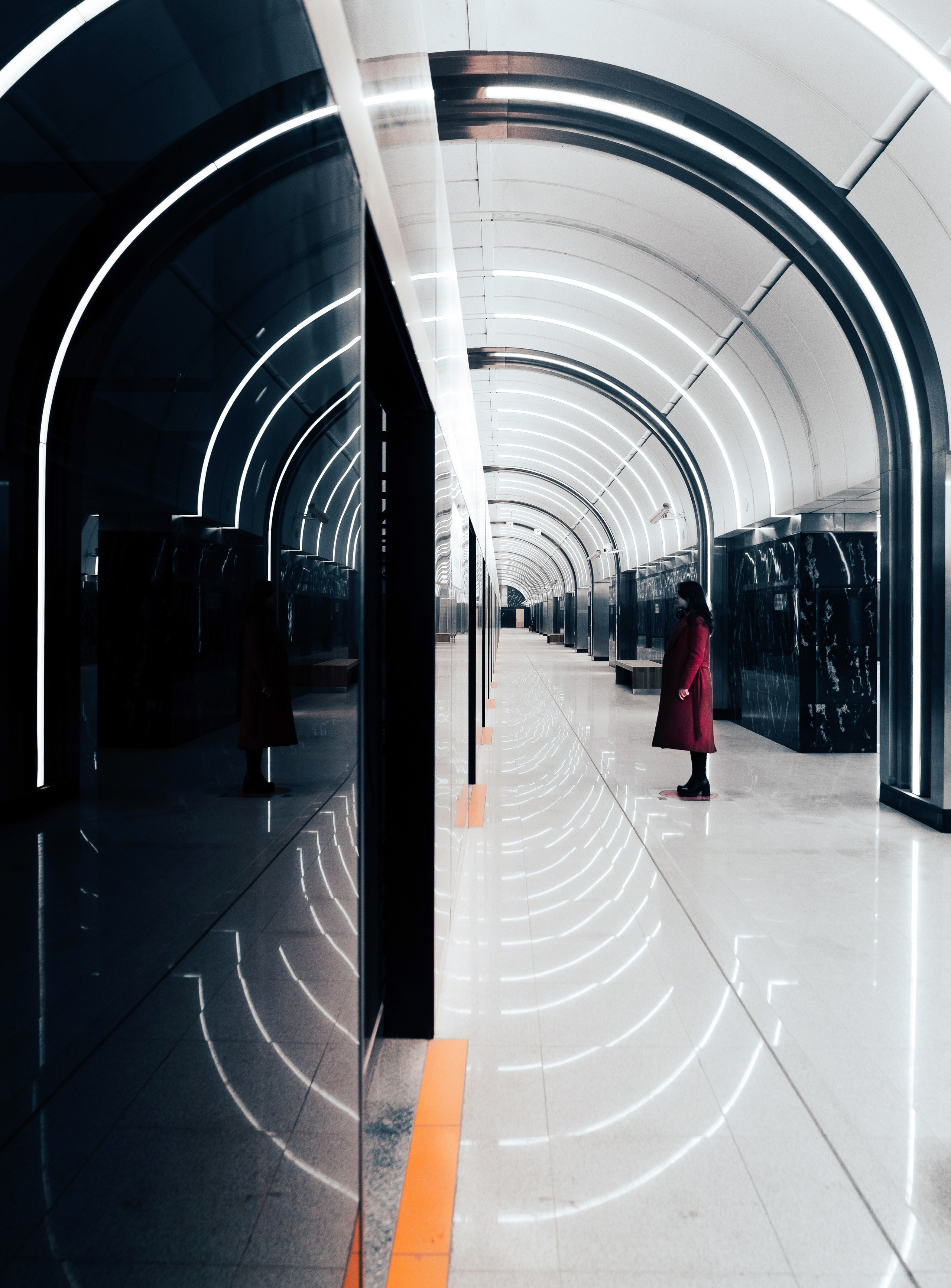 Метро СПБ Путиловская. Зеркальное отражение девушки в стильном красном пальто на платформе новой станции метро СПб, мраморные арки и неоновая подсветка, street-фотография.