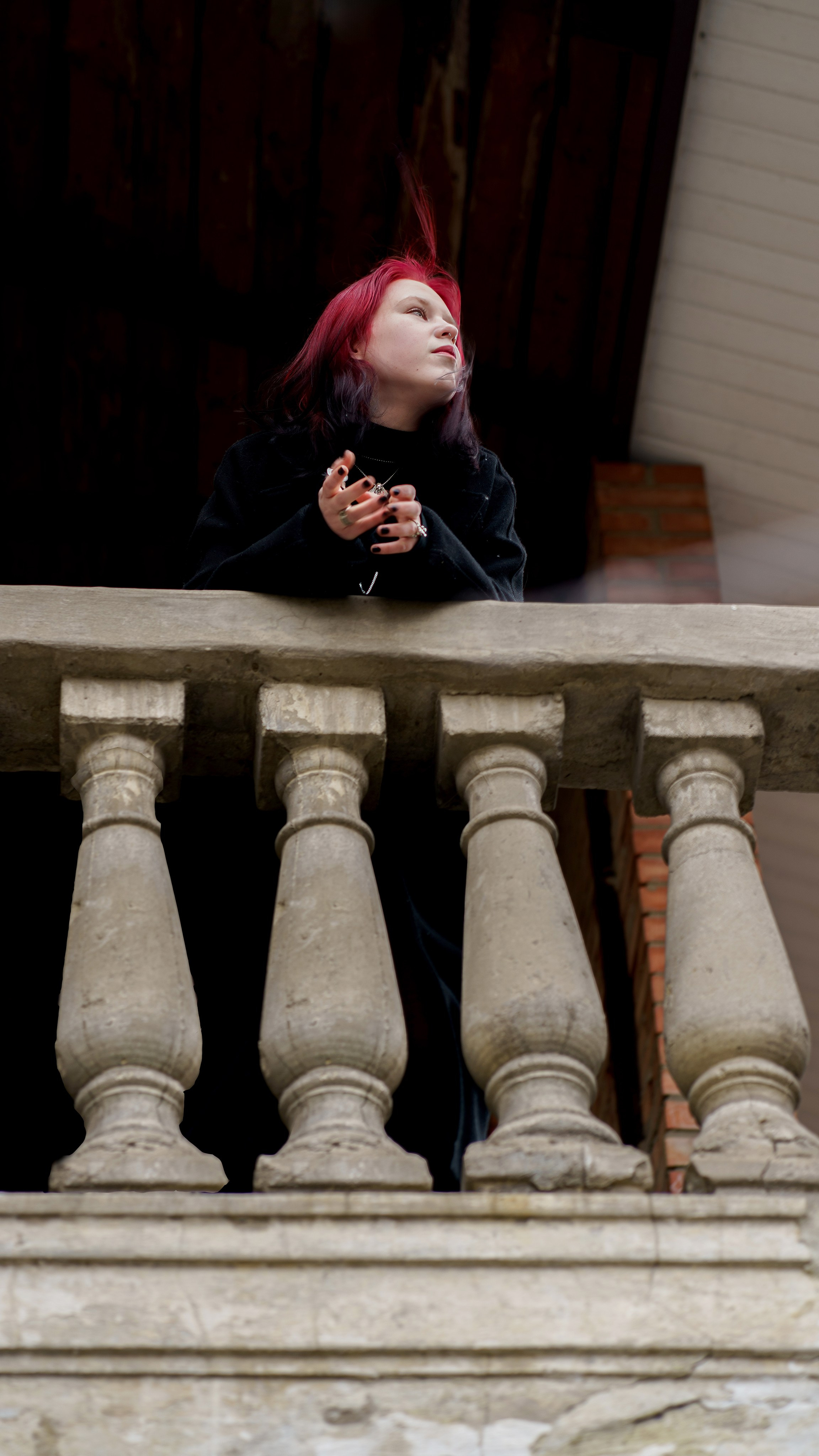 Девушка в черном пальто, с красными волосами - смотрит вдаль, опираясь на перила