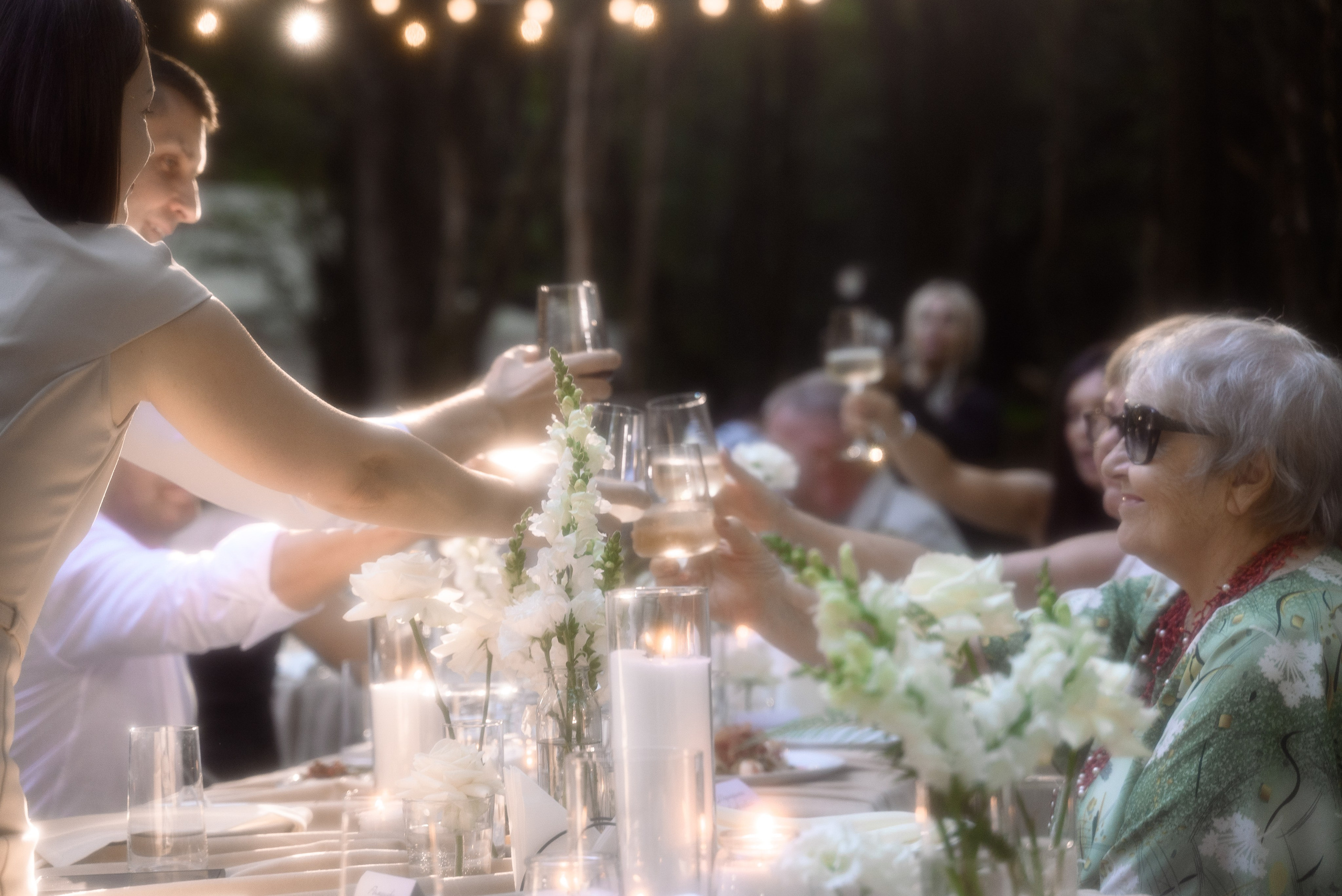 Гости сидят за свадебным столом в лесу поднимают бокалы и стукаются 