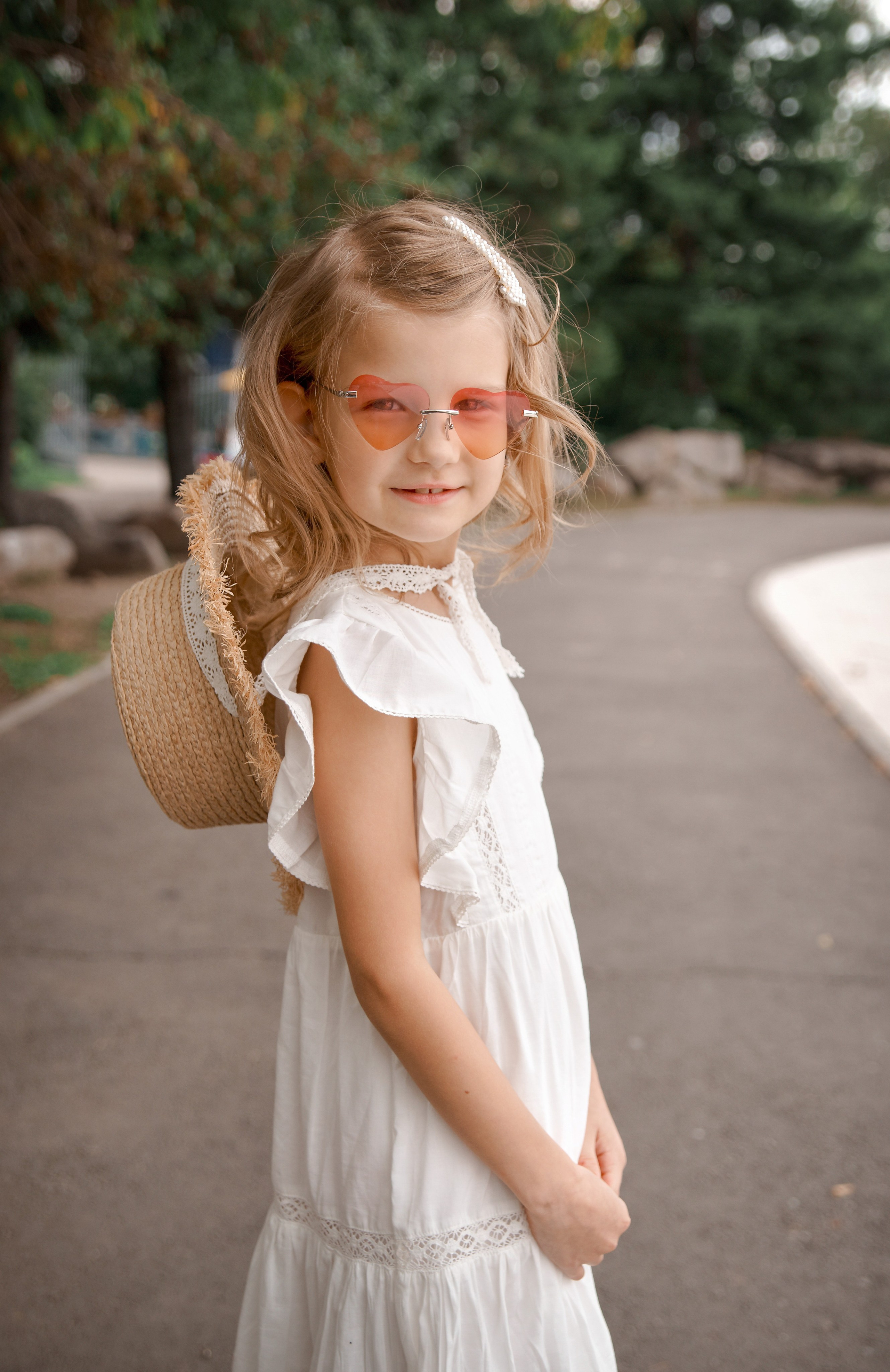 Детская фотосессия летом - девочка стоя со шляпой за спиной