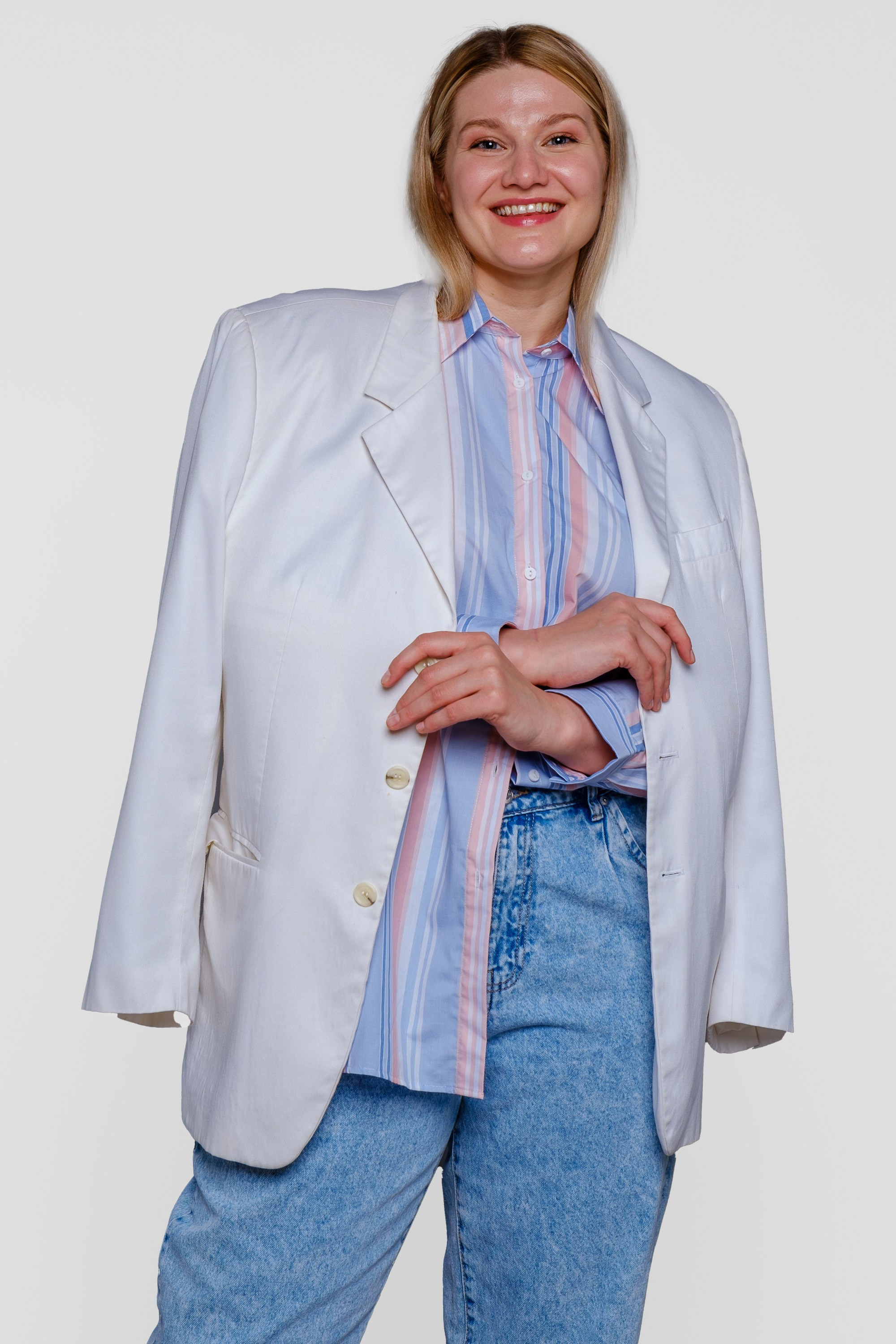 Девушка оверсайз в белом пиджаке, накинутом на плечи и голубых брюках. Вид спереди. Фото для маркетплейсов