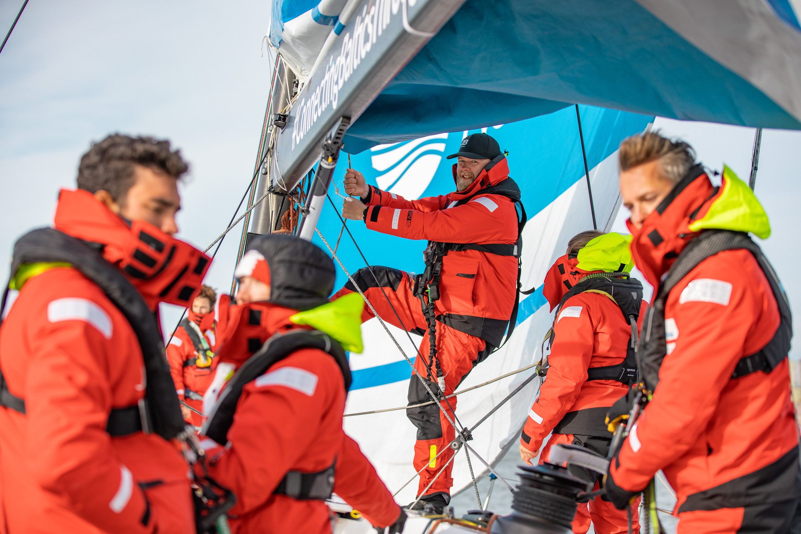 Парусная команда из Финляндии в красных непромокаемых костюмах совершает маневр на яхте.