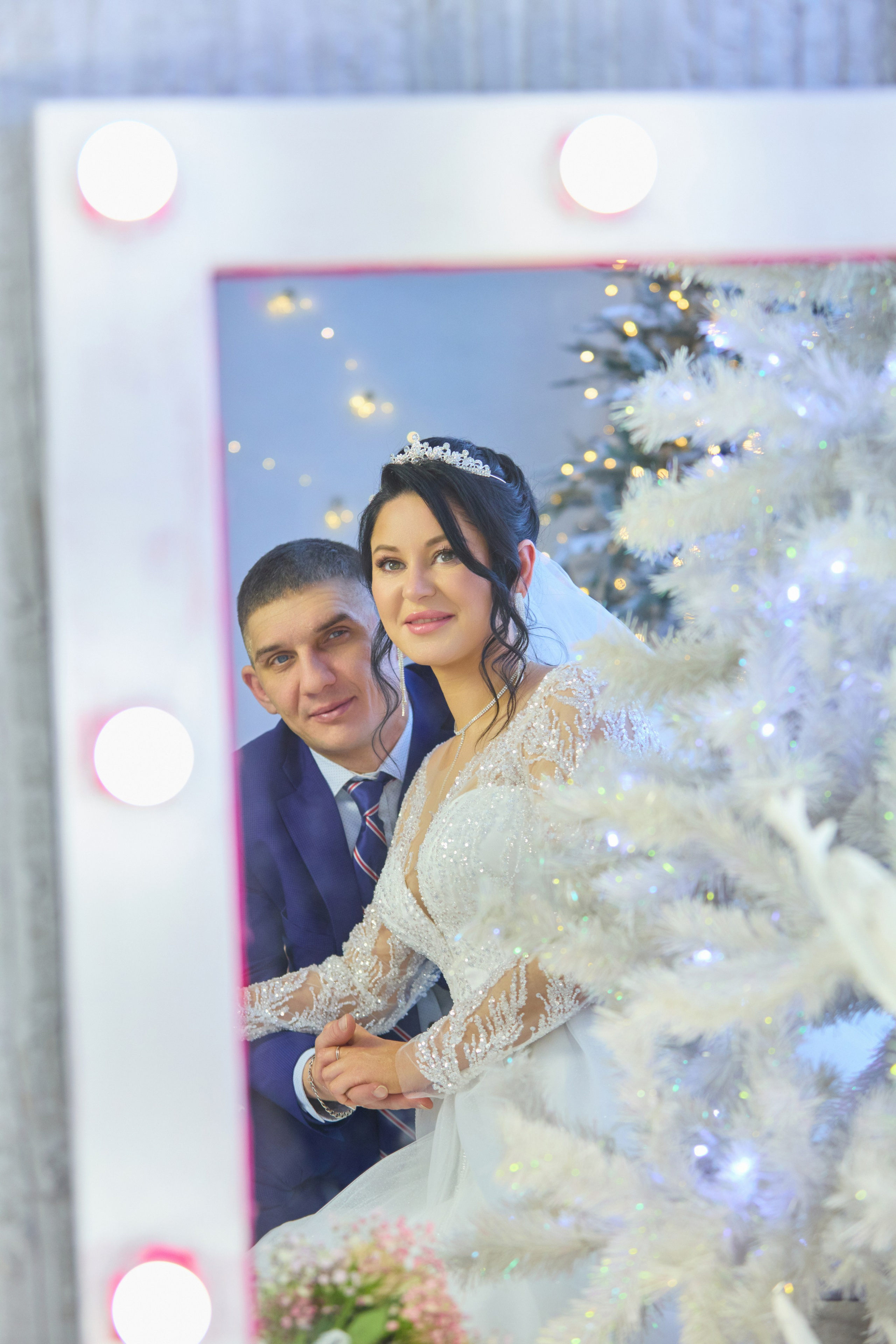 Жених с невестой в отражении большого зеркала спереди елка