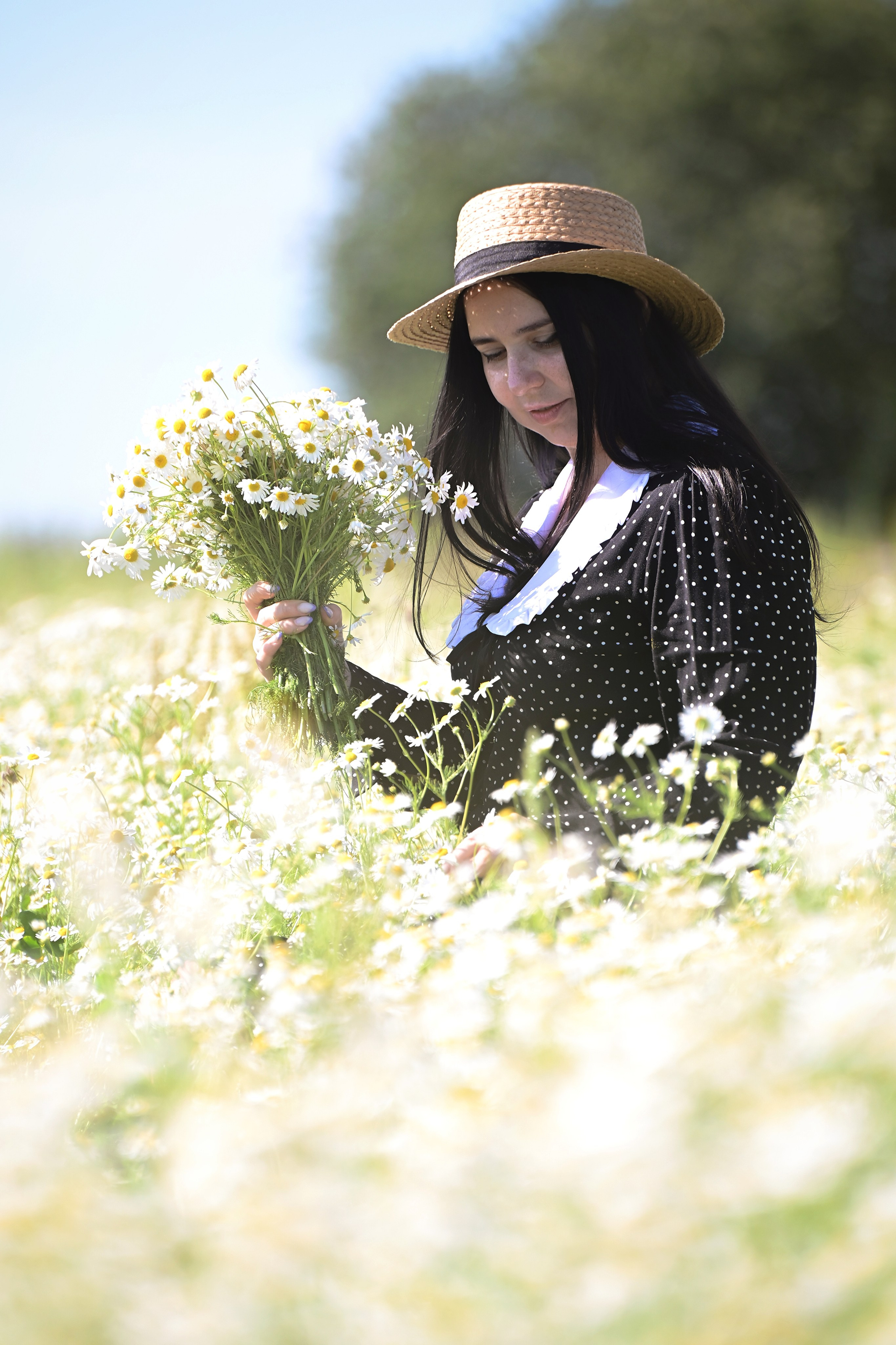 Девушка в шляпе в поле в шляпе с букетом ромашек