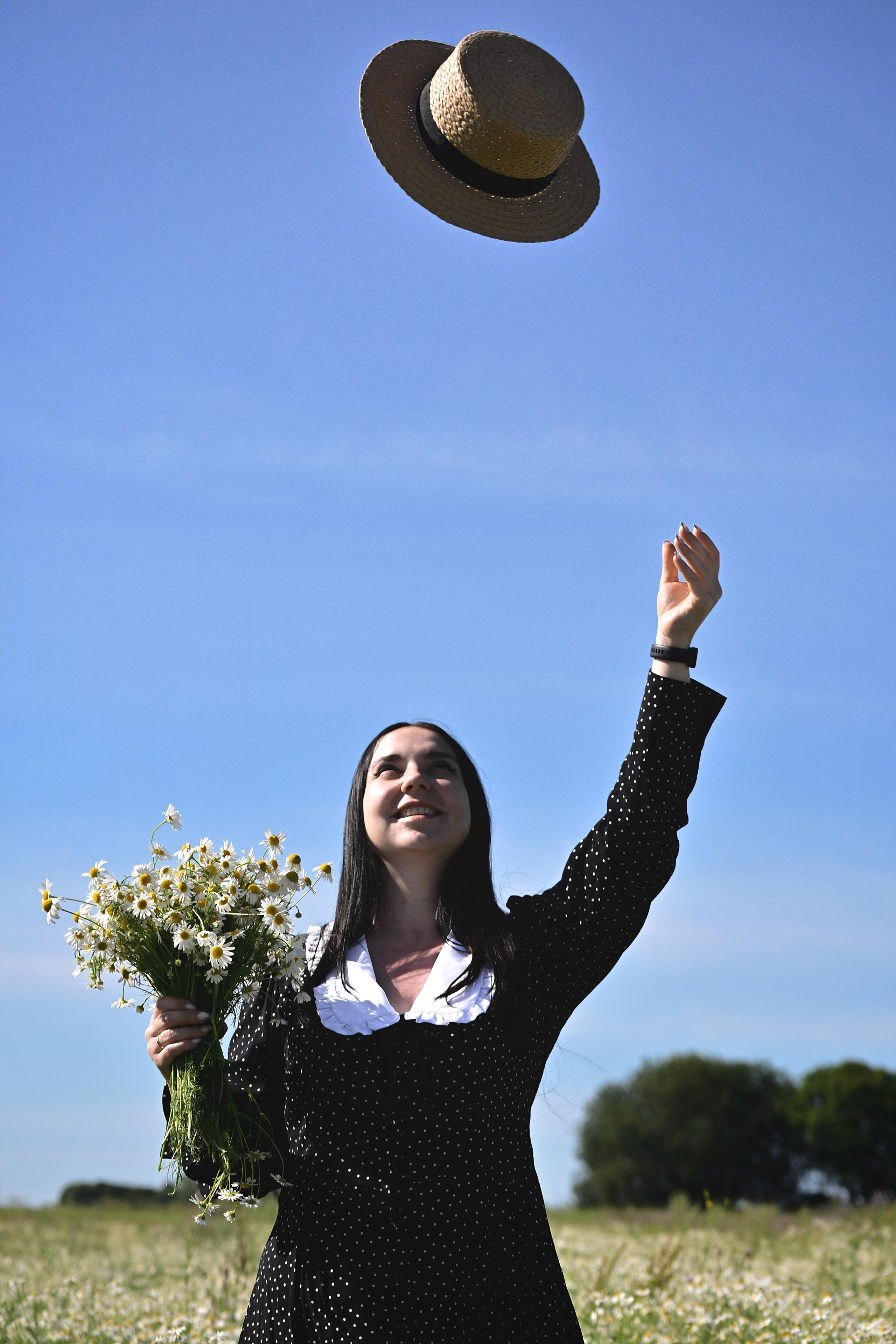 Девушка с букетом ромашек бросает в небо шляпу