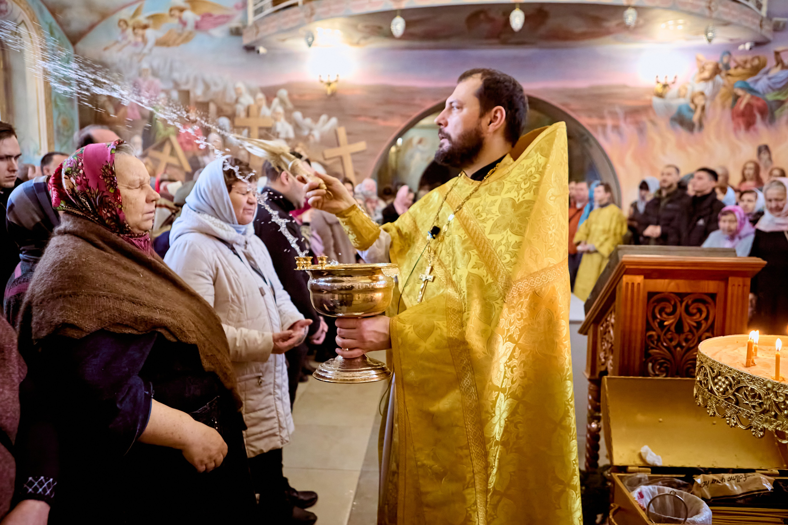 Священник окропляет святой водой прихожан после молебна