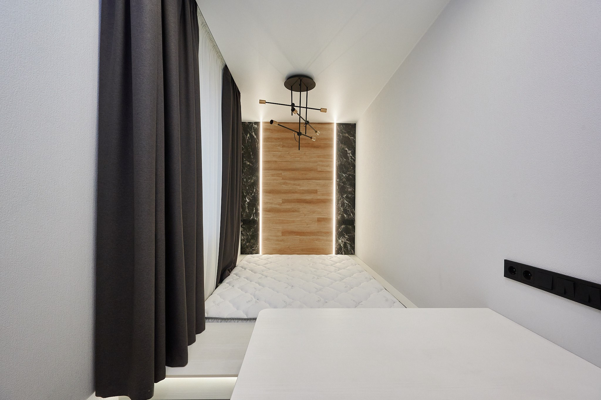 комната белые обои серые шторы белая кровать входная светло коричневая дверь 