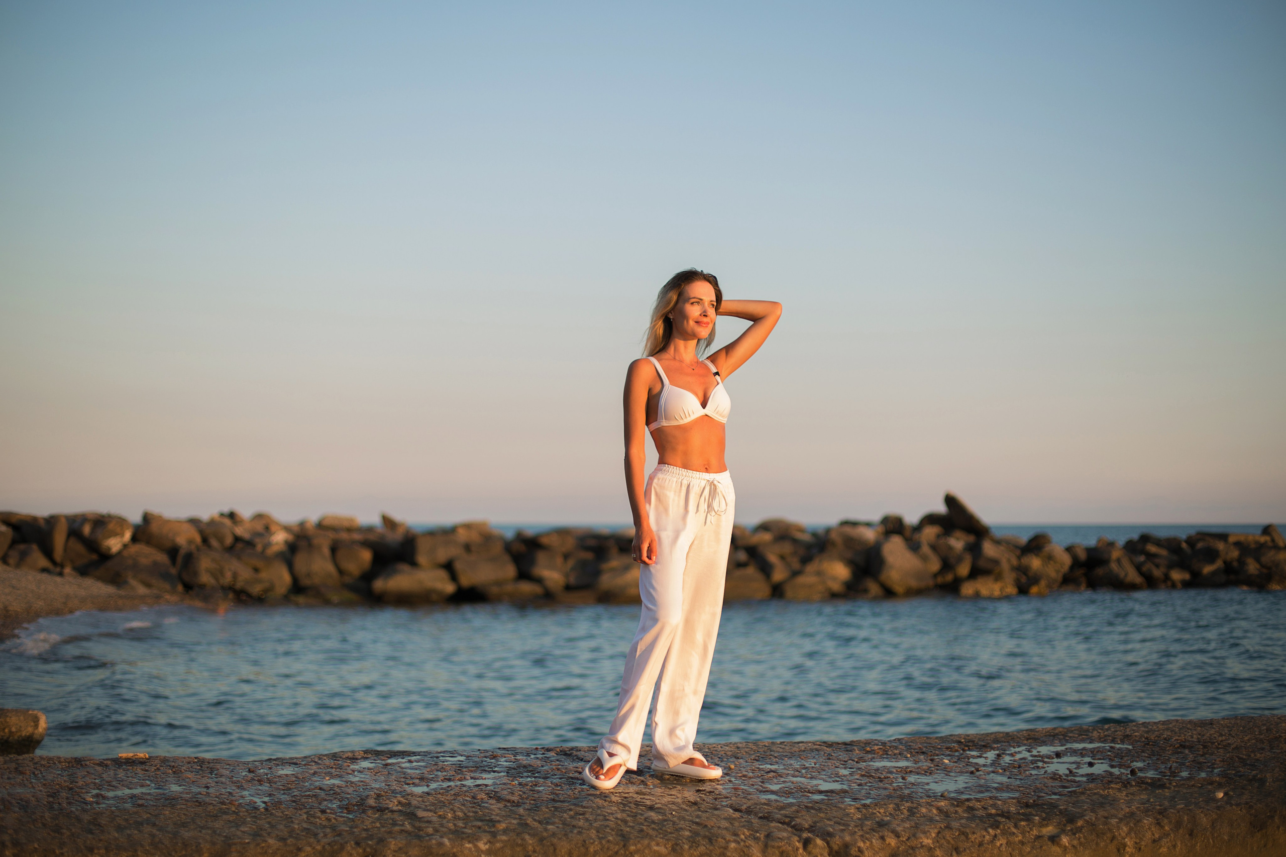 девушка в белой одежде стоит на пирсе у моря на закате