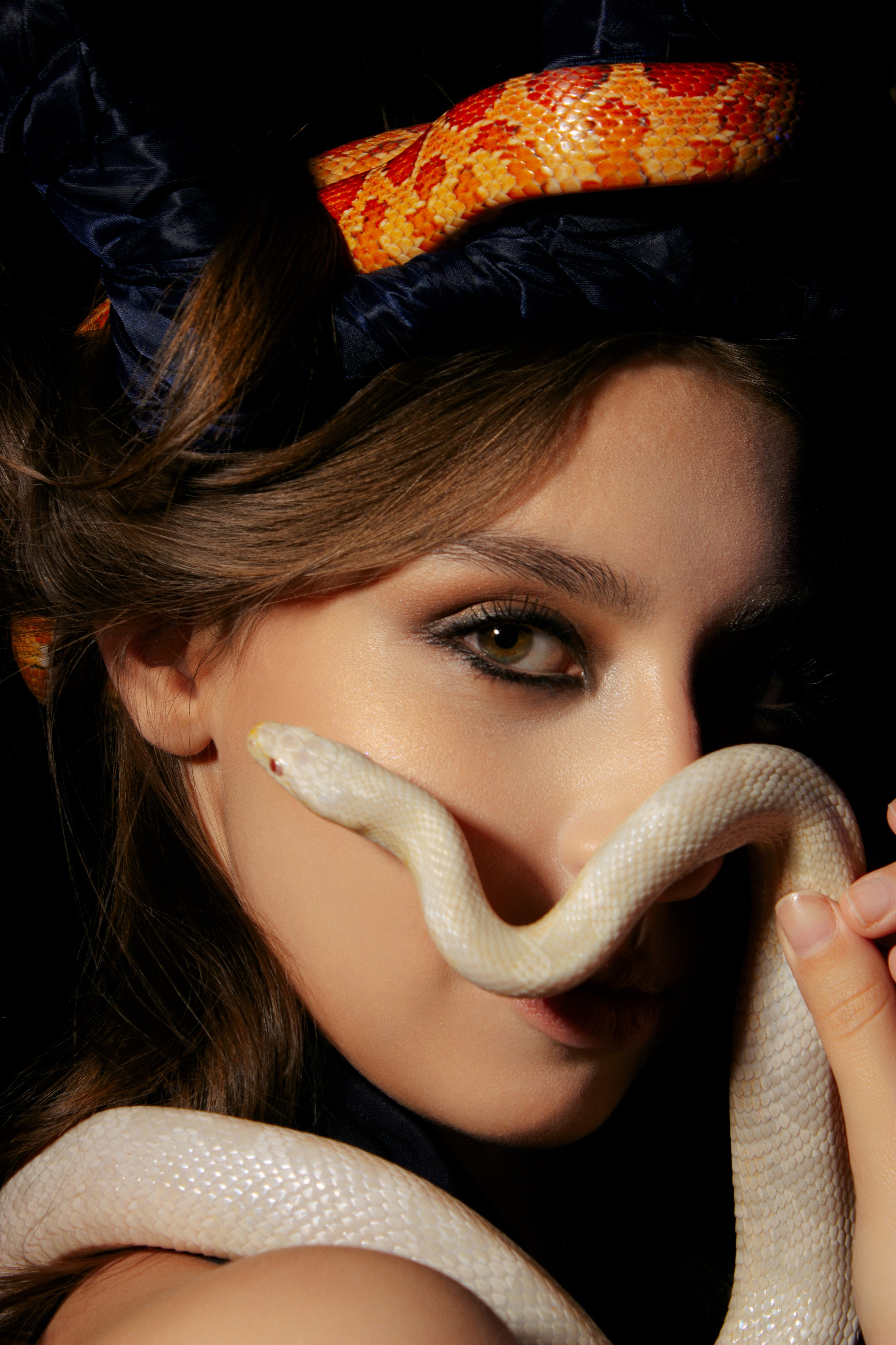 портрет девушки на черном фоне, в руках возле лица девушка держит змею