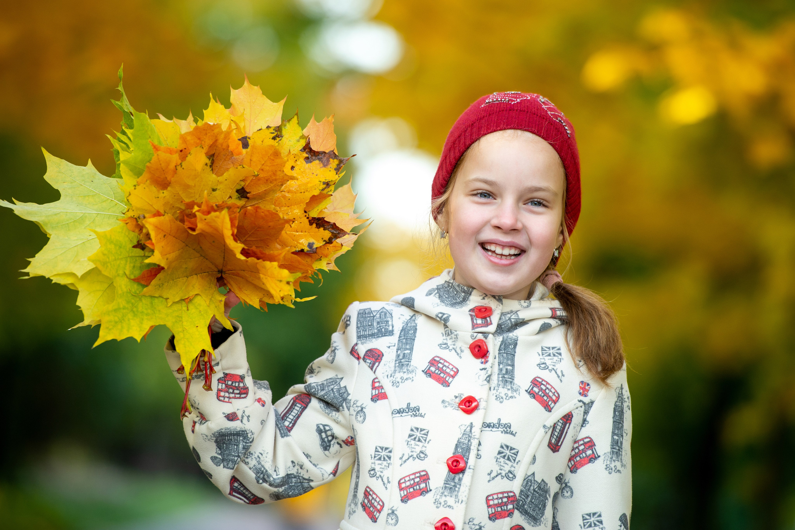 Девочка в красной шапке держит букет осенних листьев