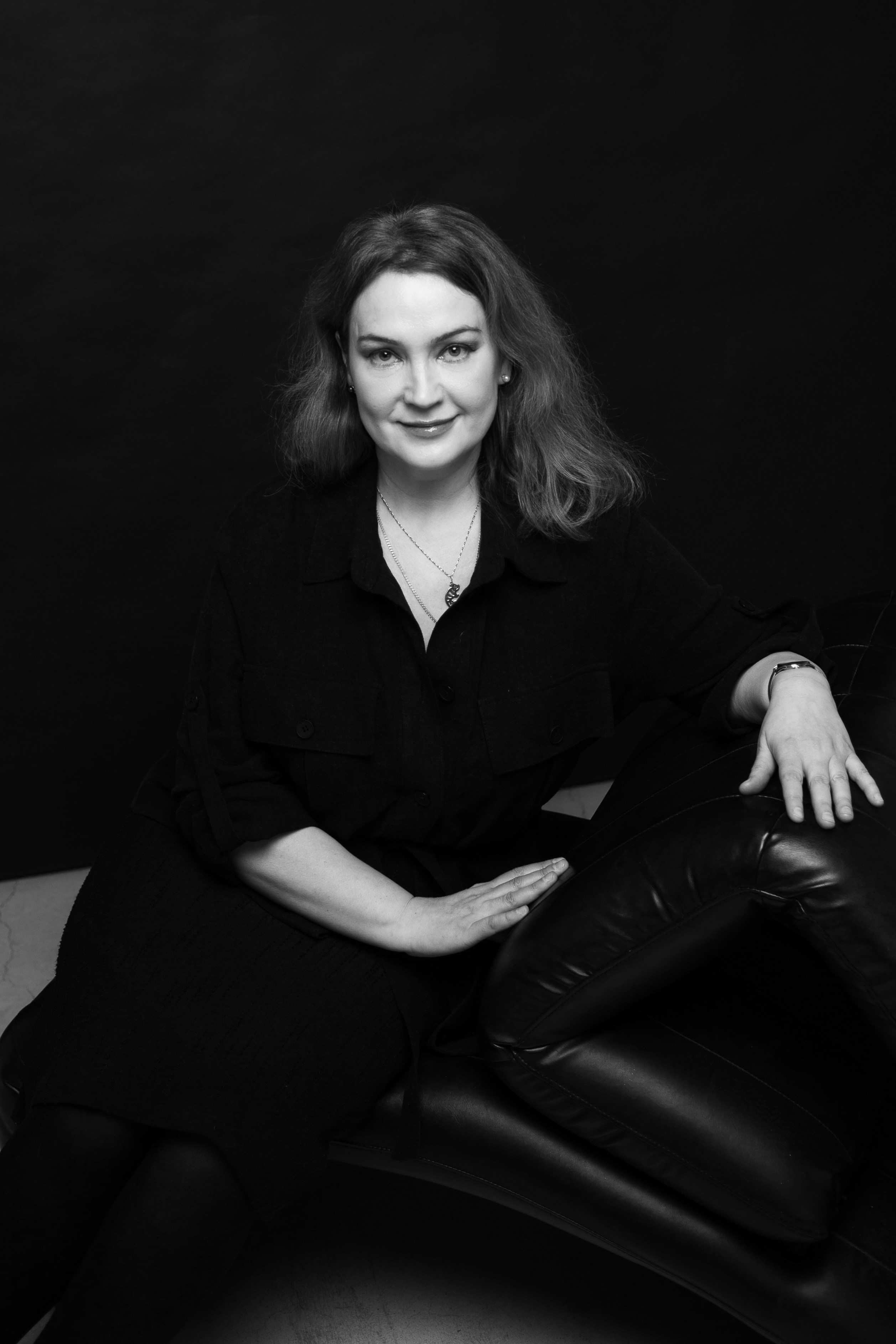 Черно-белый портрет с улыбкой, женщина сидит на темном фоне, минималистичная студия Санкт-Петербург