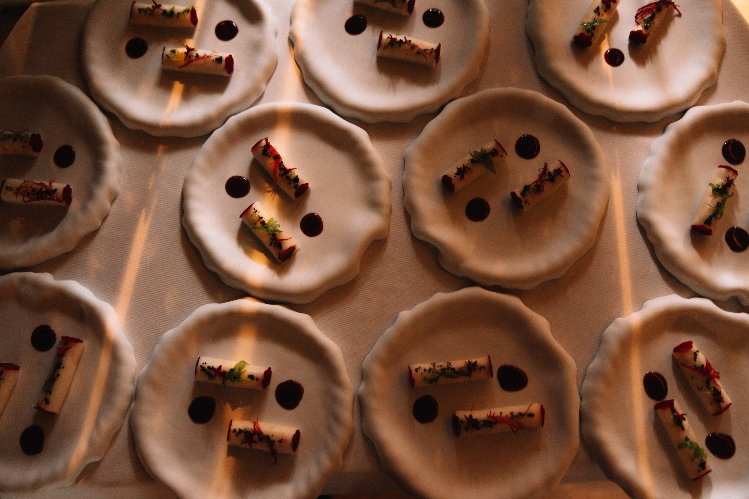 Раскладка: Вид сверху на сет одинаковых закусок на белых блюдцах, геометричная композиция.