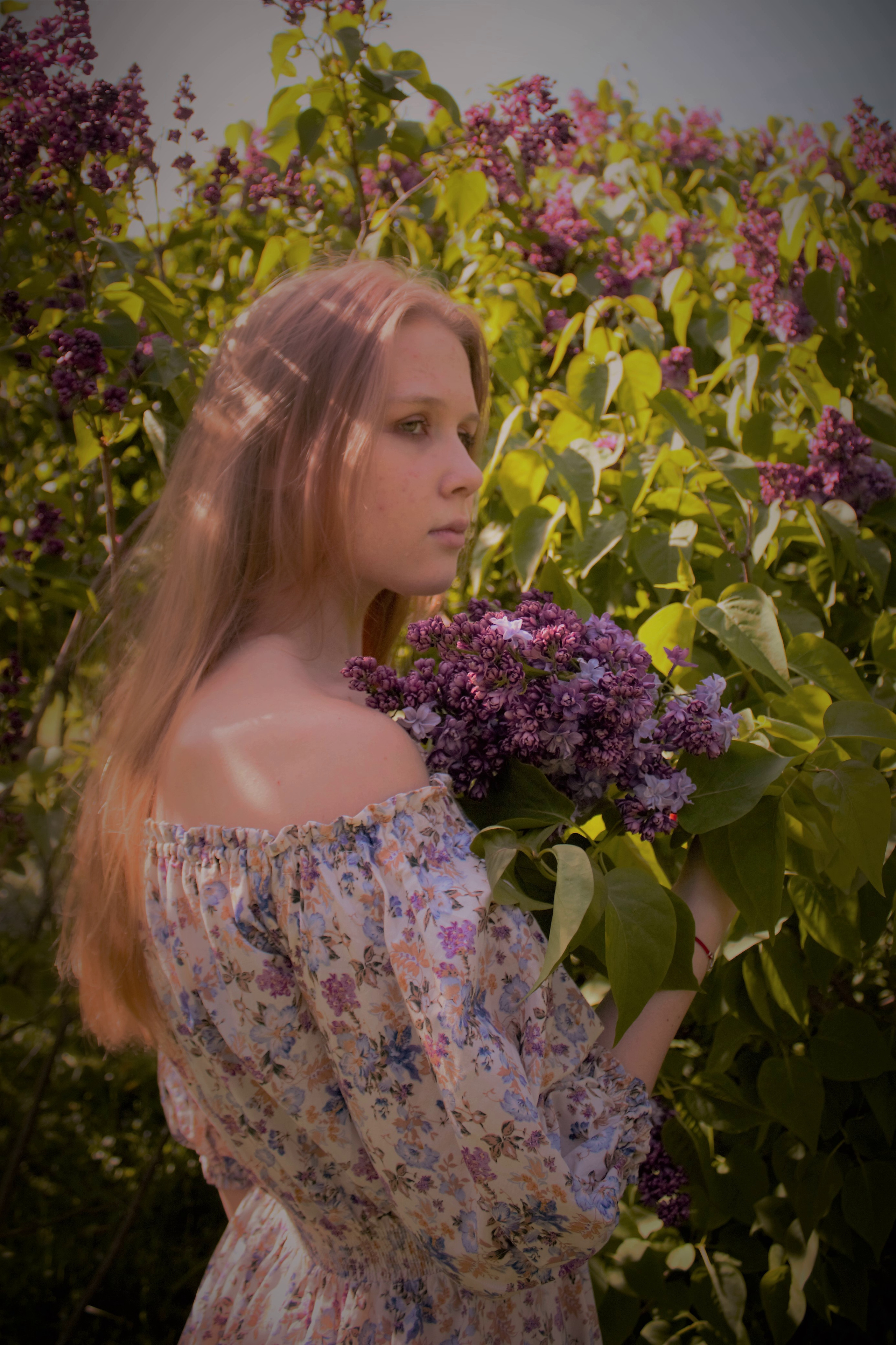 Девушка с длинными волосами держит в руках сирень.