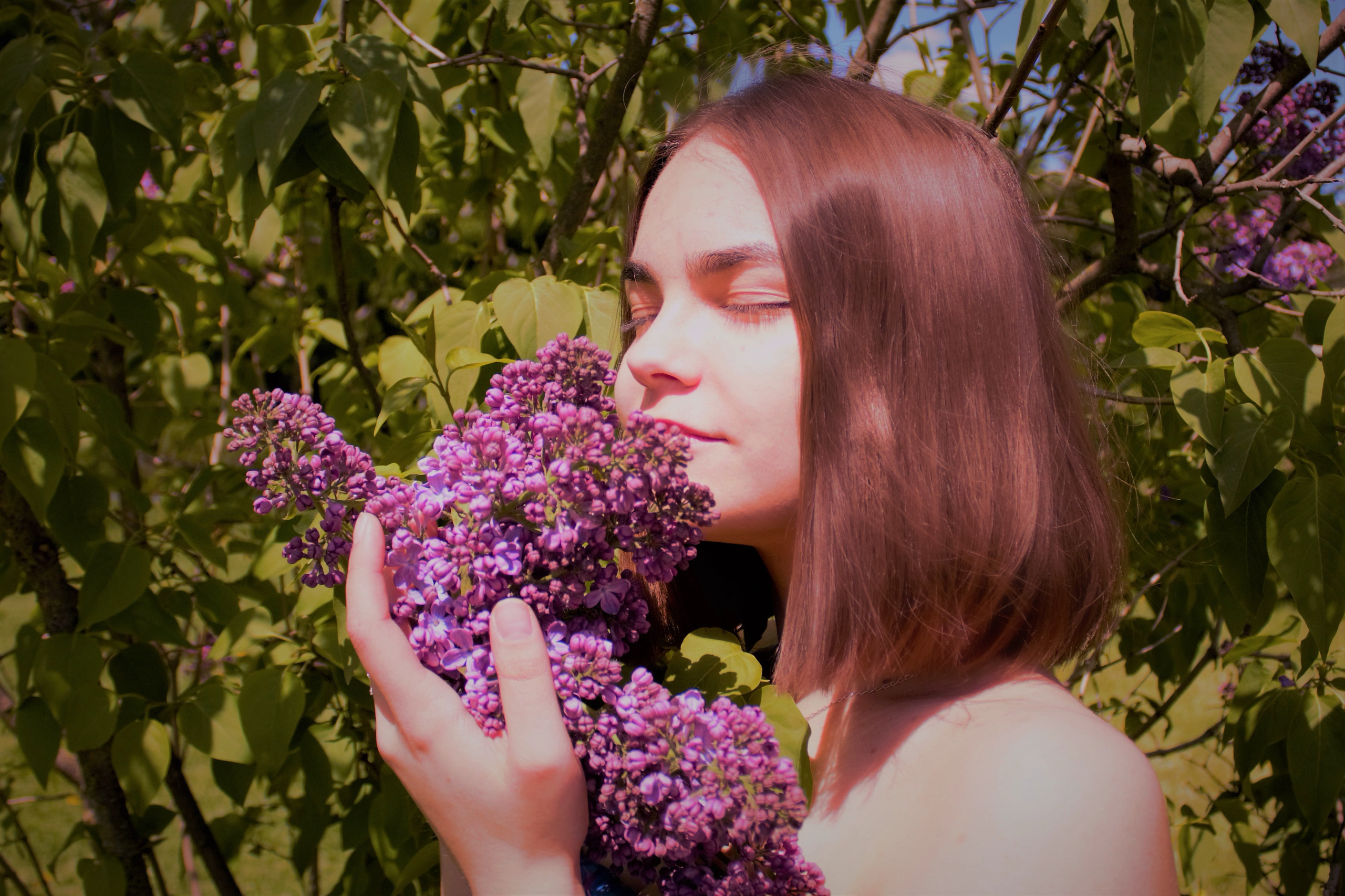 Девушка брюнетка держит в руках гроздь сирени.