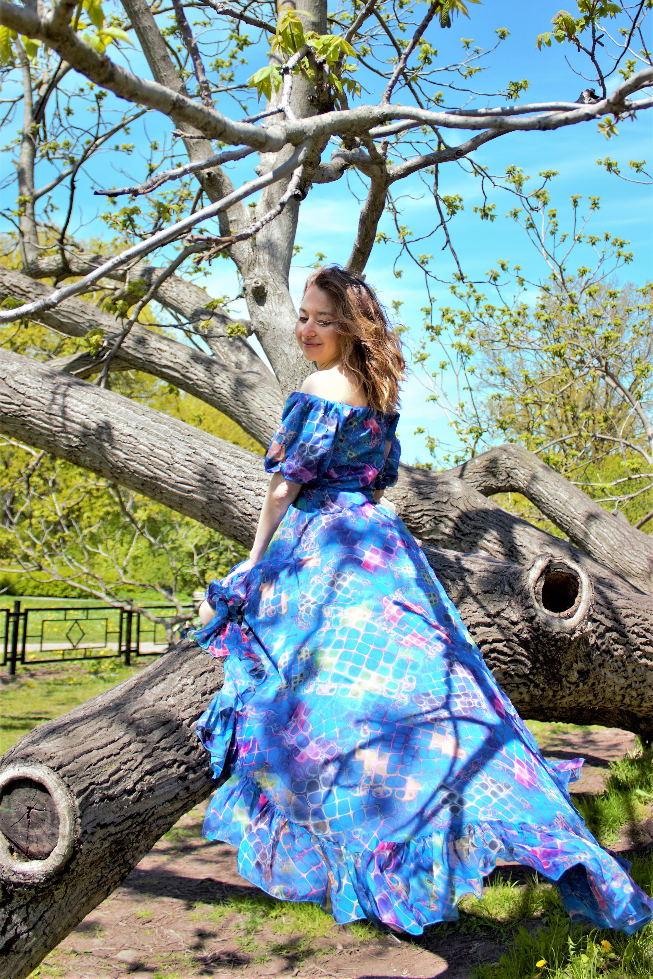 Девушка  в синем платье сидит на ветке дерева.