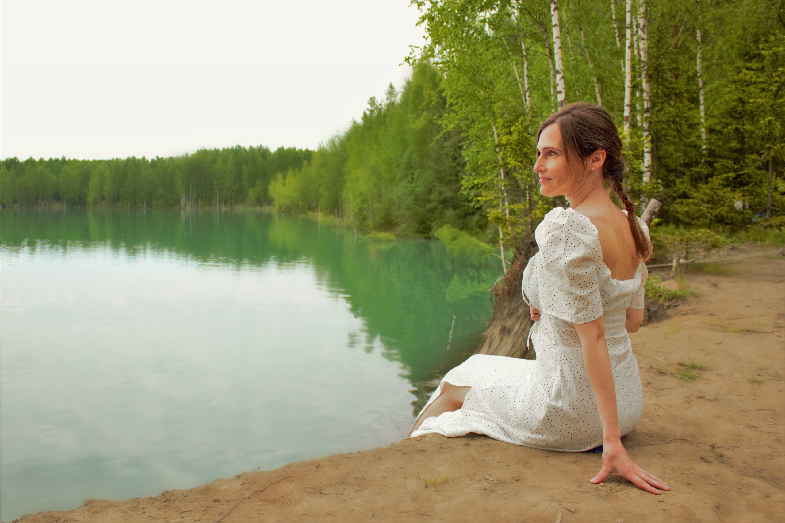 Девушка сидит на берегу озера и смотрит вдаль.