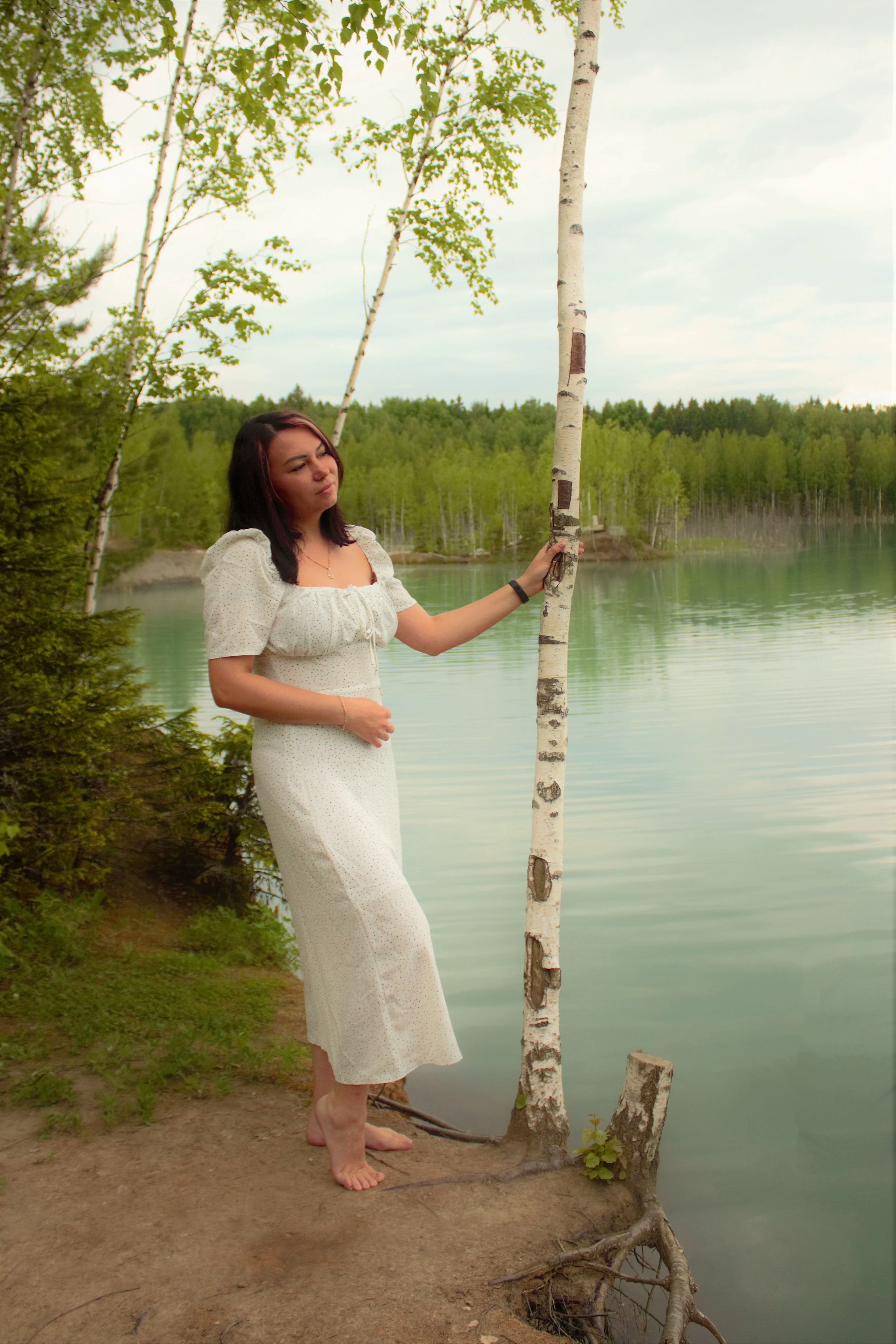 Девушка брюнетка в белом платье на берегу голубого озера.