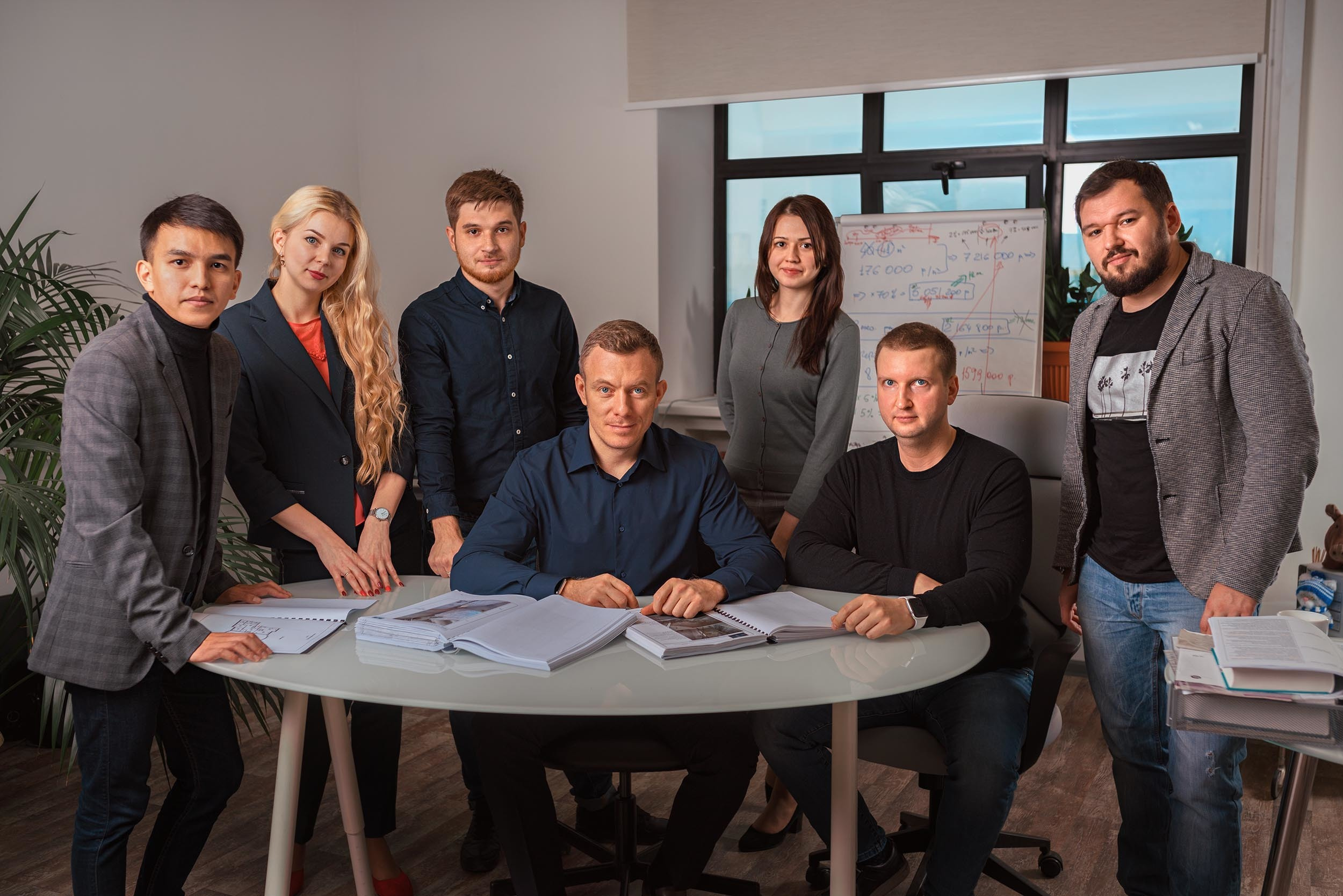 Сотрудники компании смотрят в камеру стоя за столом в офисе