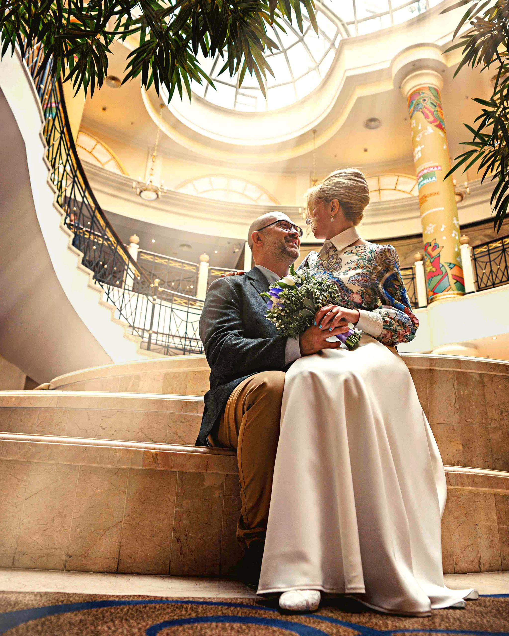 Невеста сидит на коленях у жениха в попещении со стекляным потолком