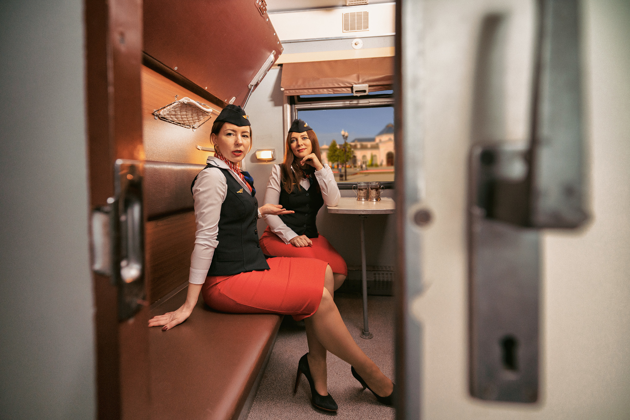 Две проводницы в красных юбках и пилотках сидят в купе поезда