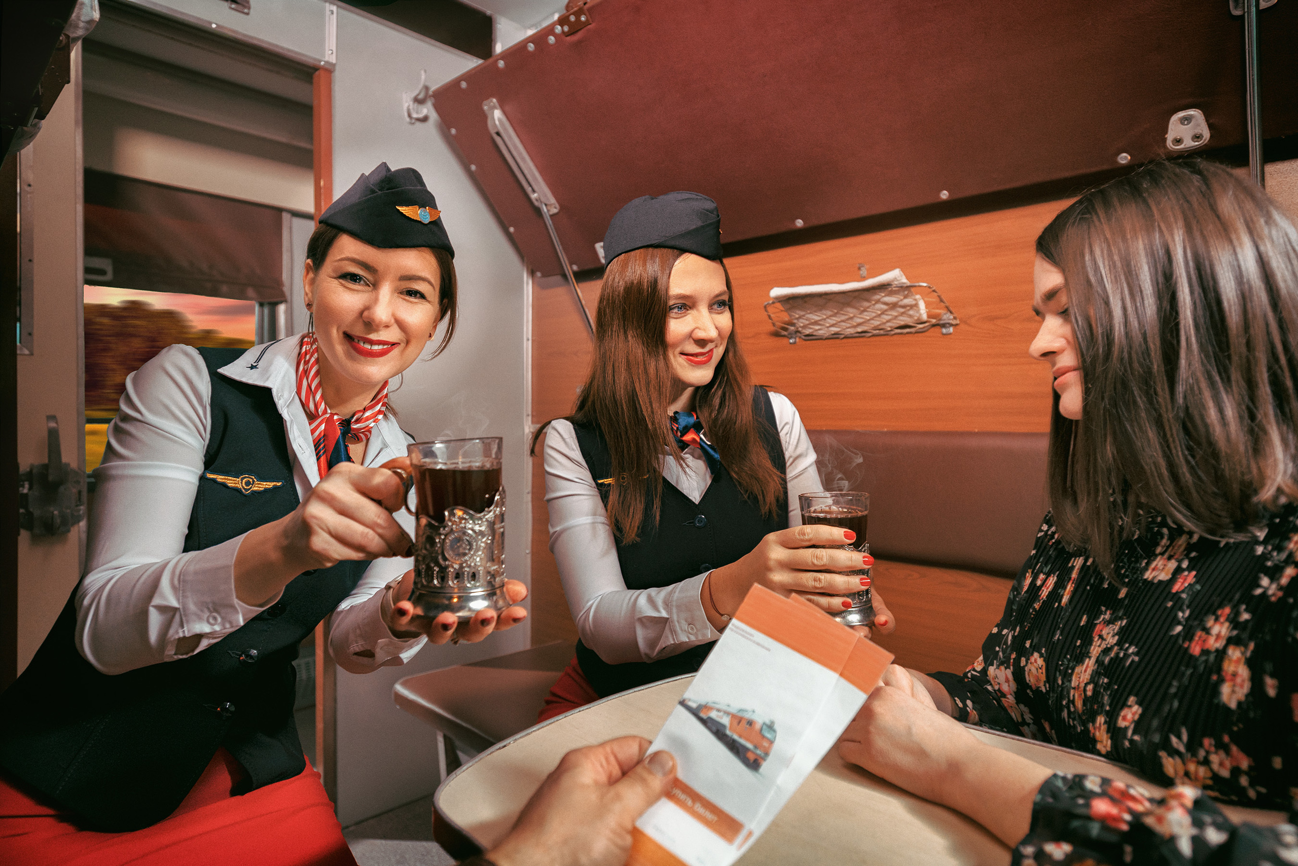 Две проводницы в красных юбках и пилотках в купе поезда подают чай