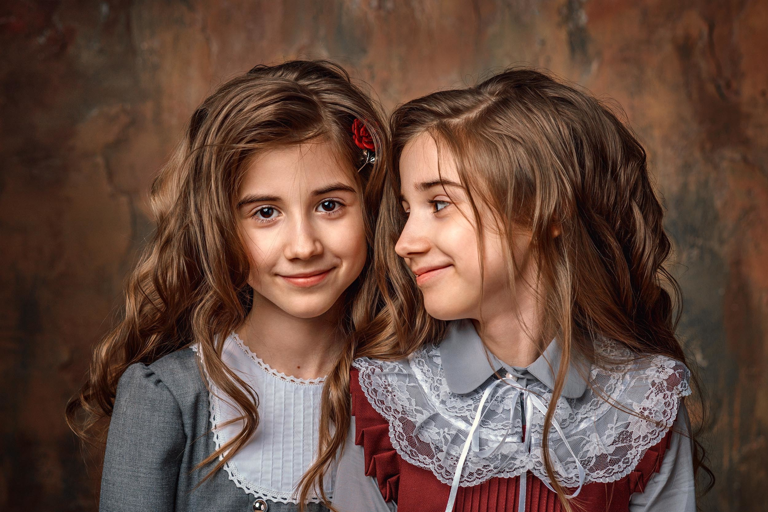 Две сестры, двойняшки с длинными волосами в красивых платьях, одна смотрит назрителя, другая на сестру